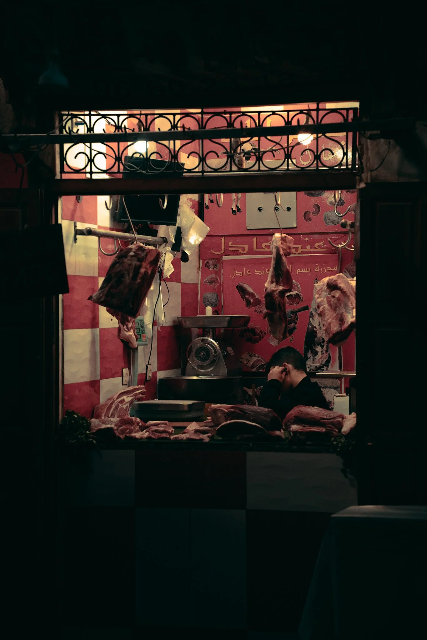Eine Metzgerei mit Fleischstücken, die im Fenster displayiert sind, und einem Mann im Hintergrund, der telefoniert.