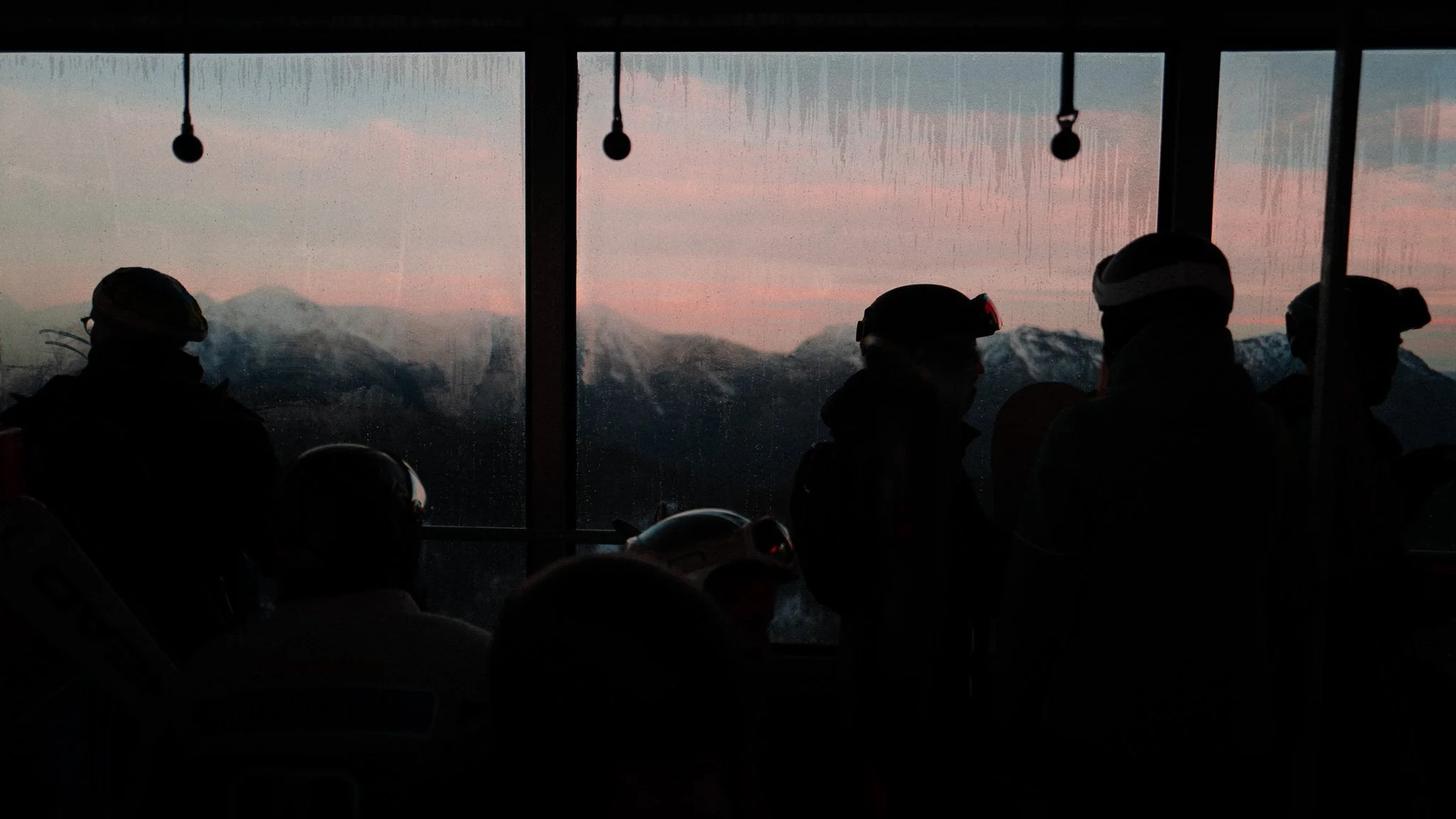 Menschen in Skihütte oder Gondel mit Sicht auf verschneite Berggipfel bei Sonnenuntergang