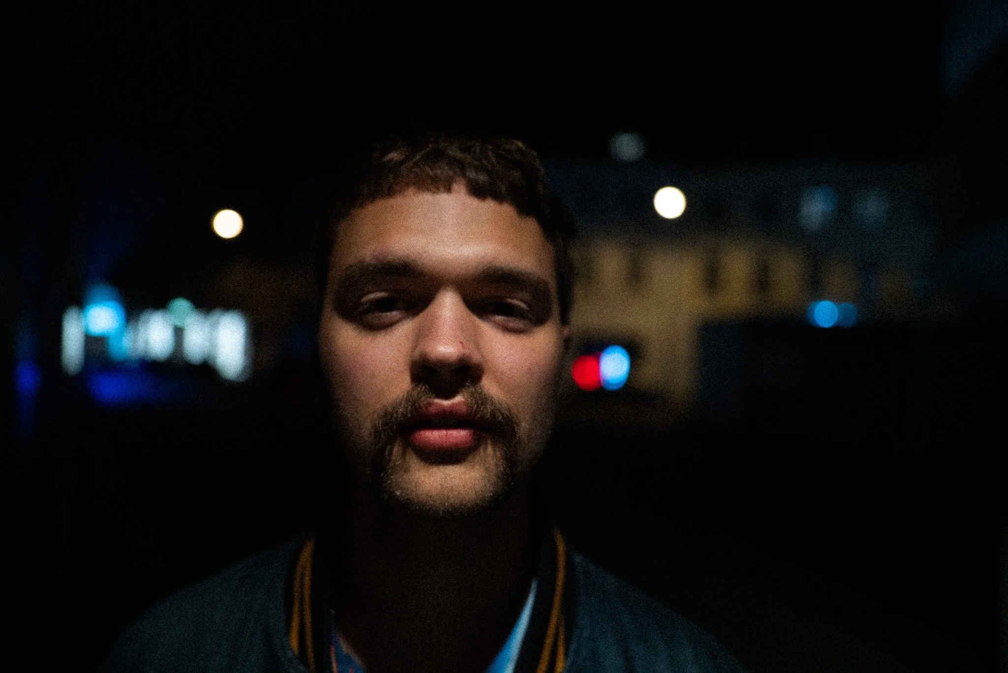 Porträt eines jungen Mannes bei Nacht, Halbaufnahme, dunkler Hintergrund mit einigen Lichtern, ruhige Stimmung.