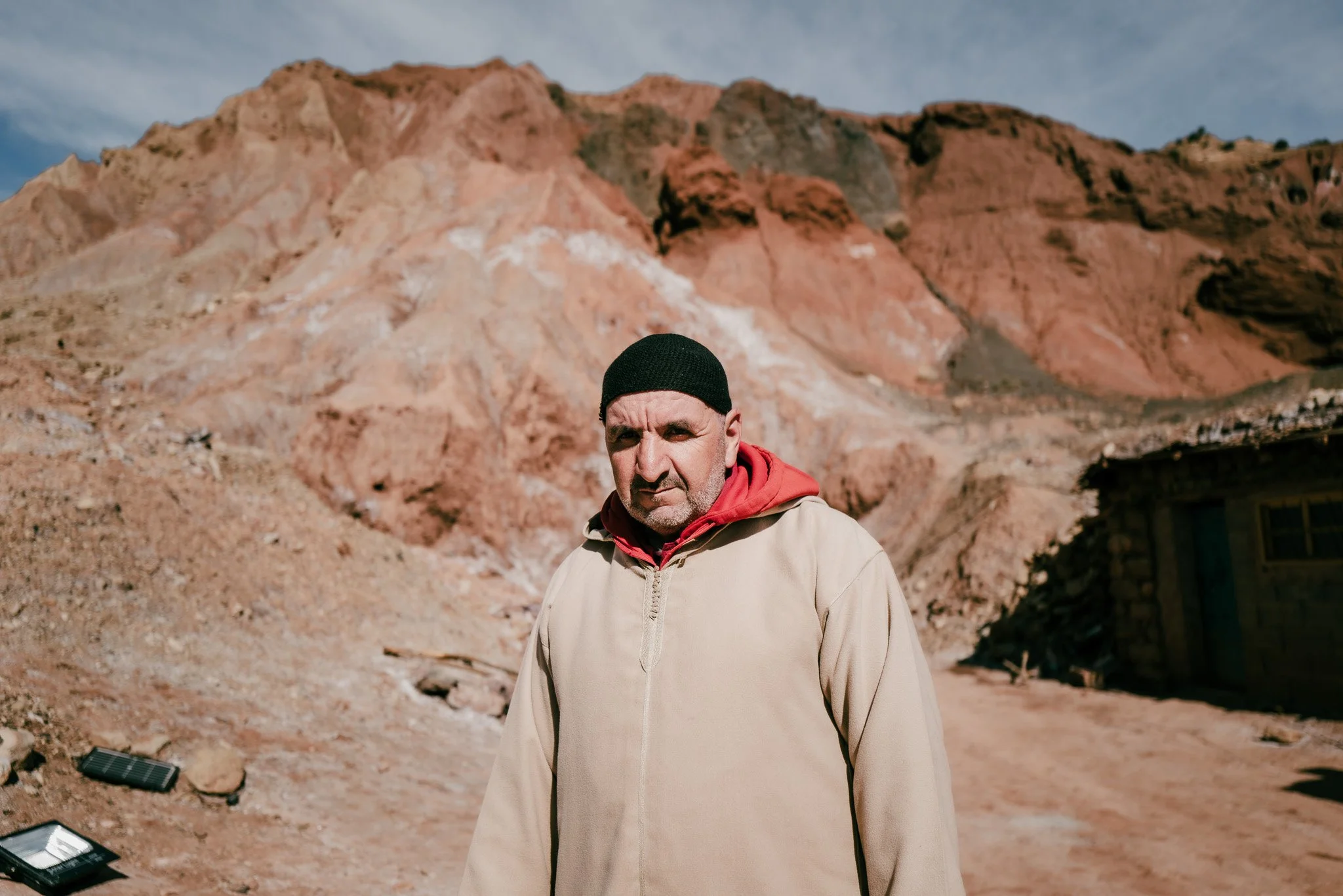 Mann in beige Jacke und schwarzem Mützenkopf vor roten Felsen in der Wüste