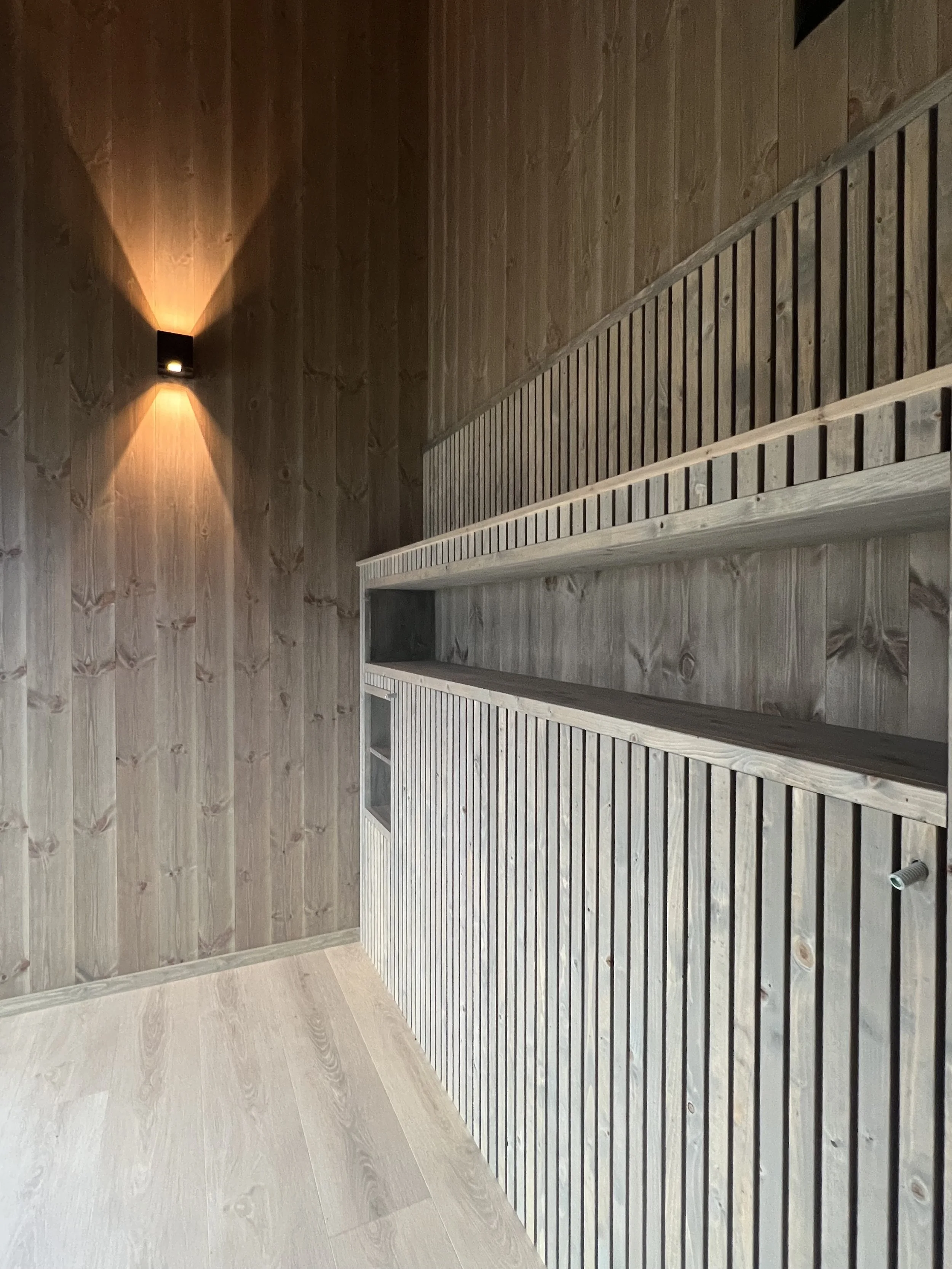 Interior of a wooden sauna with a wall sconce lighting and wooden bench seating.