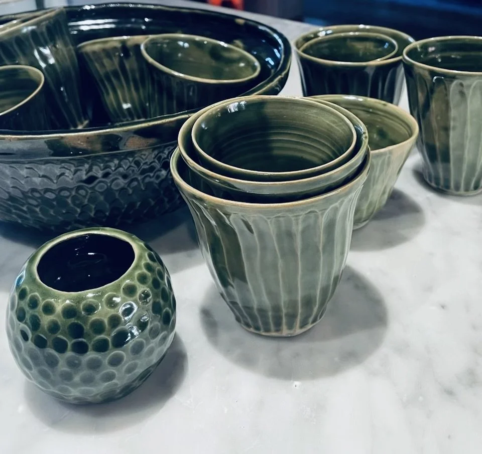 A collection of green ceramic bowls and cups with vertical ribbed patterns, placed on a white marble surface.
