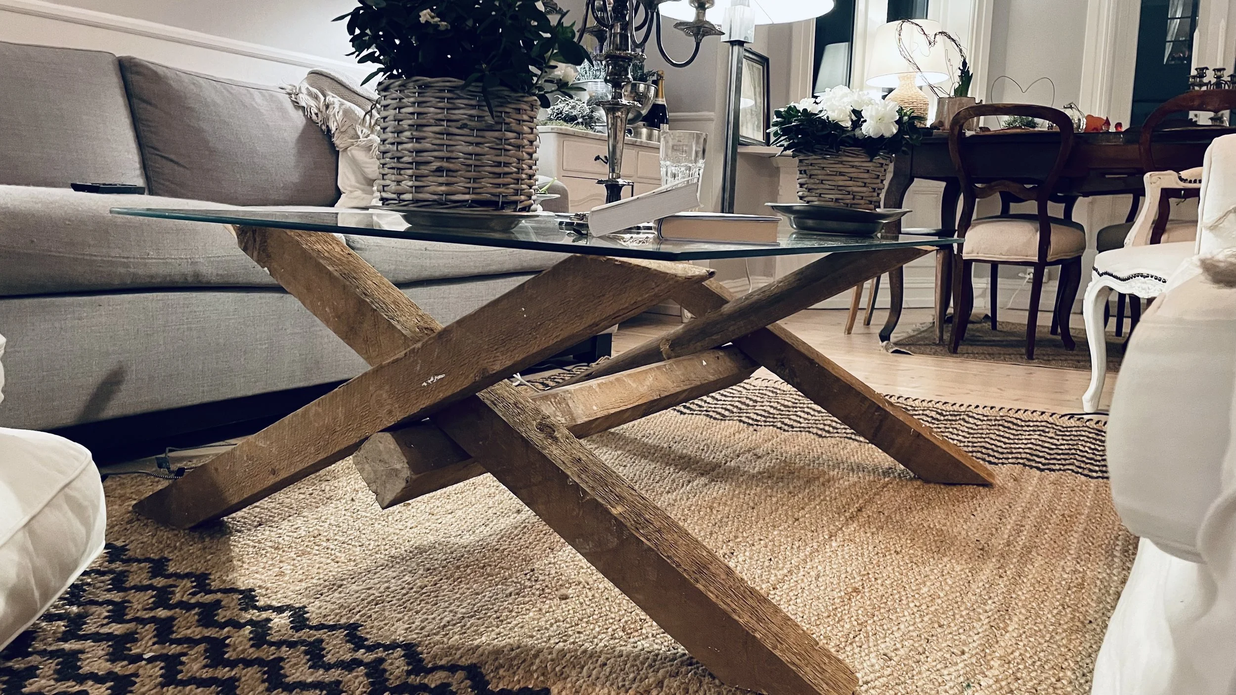 Living room with a glass-top coffee table with a wooden base, gray sofa, and a dining area in the background.