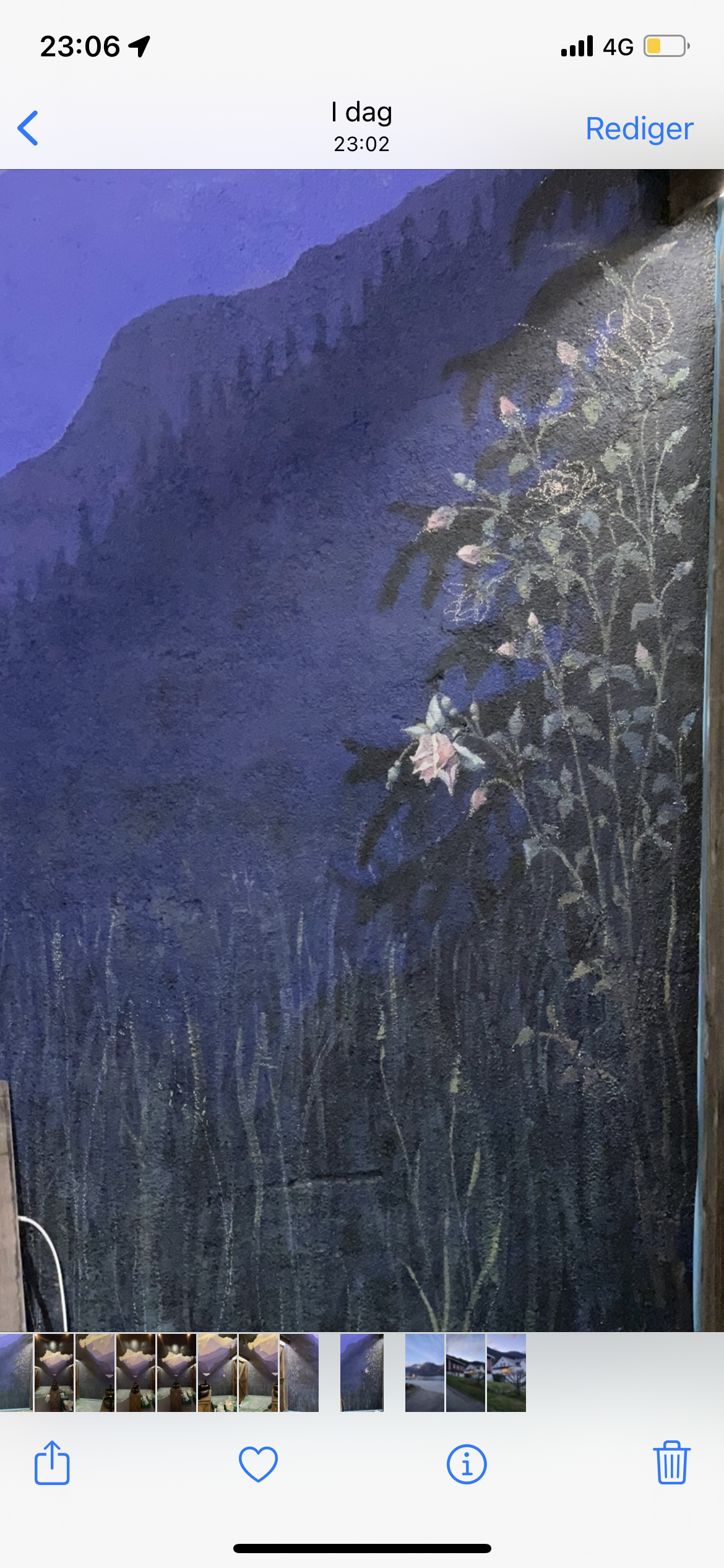 A painted mural of a mountain landscape with pink flowers and green foliage on a dark background, illuminated by purple and blue lighting.