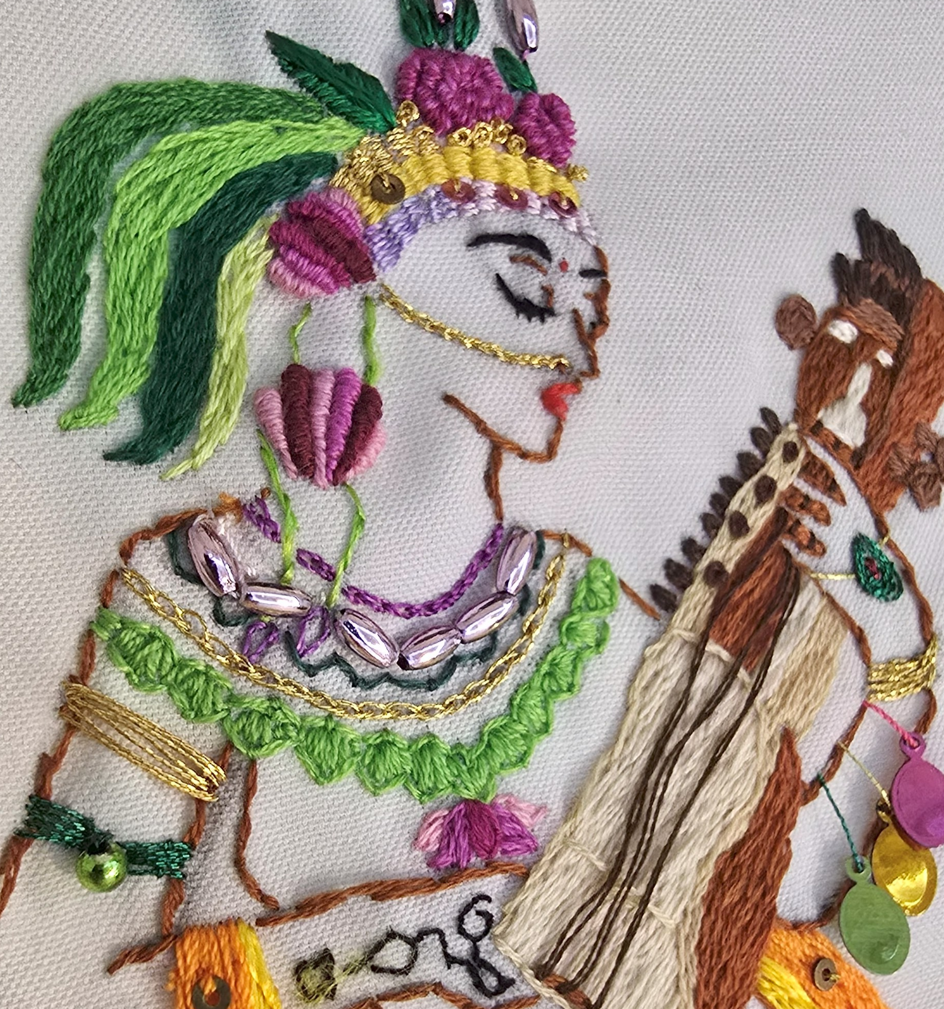 Embroidery of a woman wearing traditional attire with a headpiece, jewelry, and a horse, featuring colorful thread and bead details.