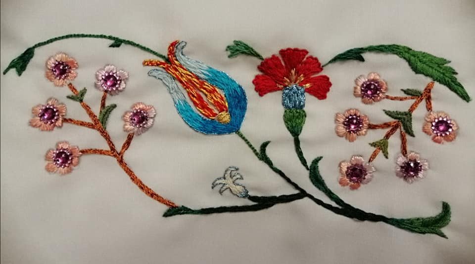 Embroidery of a colorful bird perched on a branch amid flowers.