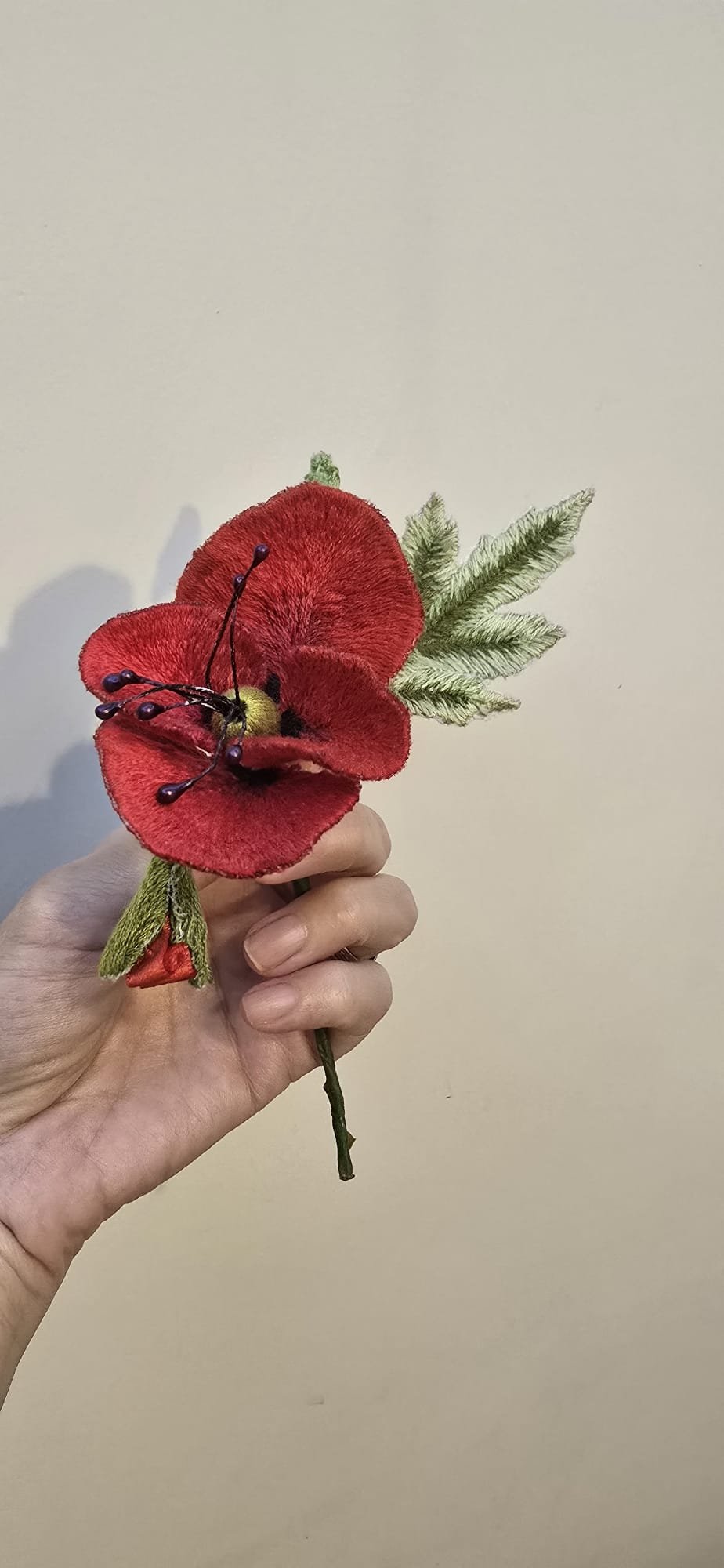 Hand holding an artificial red flower with green leaves and black-tipped stamen.