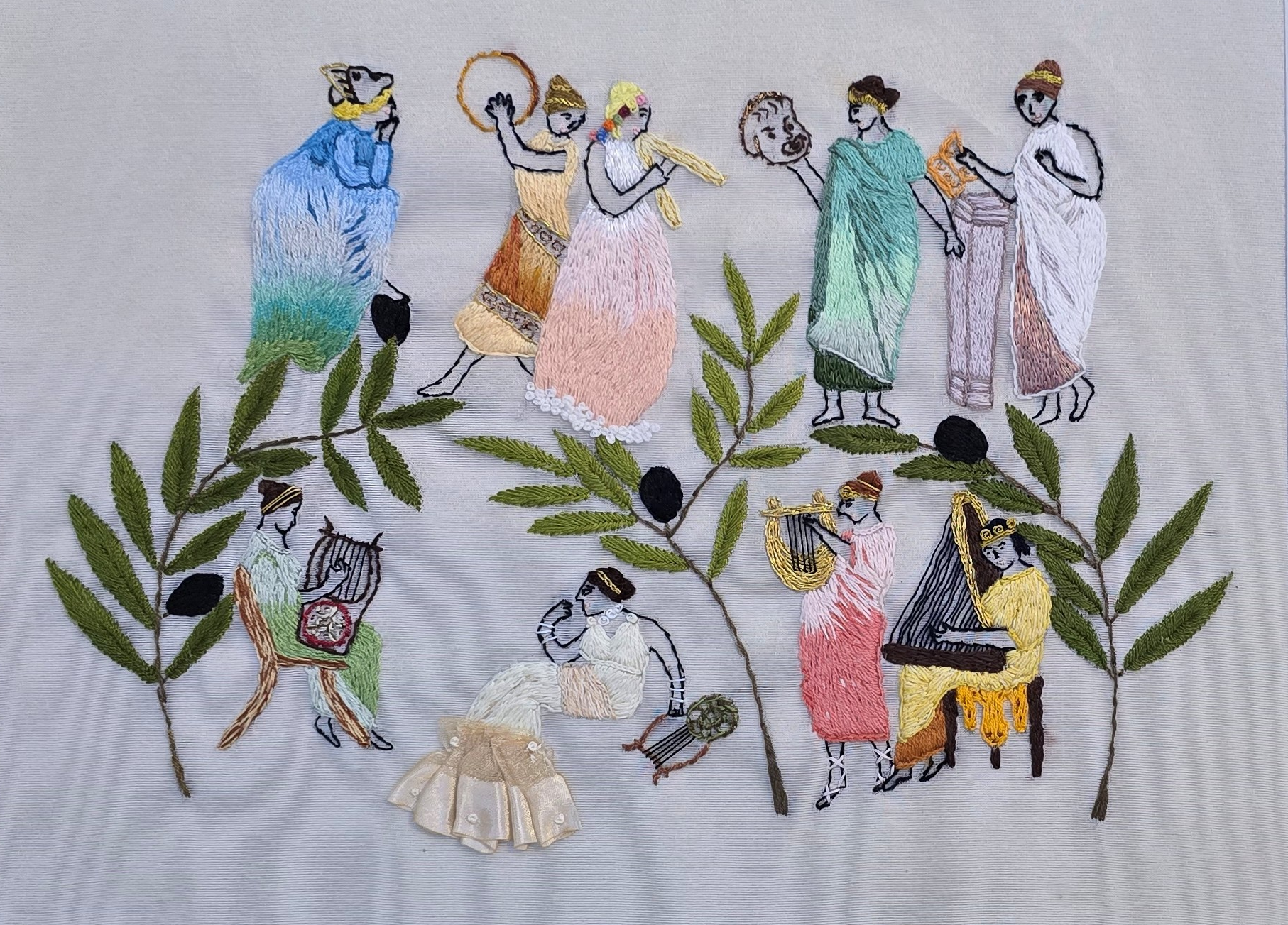 Embroidery of a scene with figures playing musical instruments, dancing, and socializing, surrounded by embroidered green leaves.