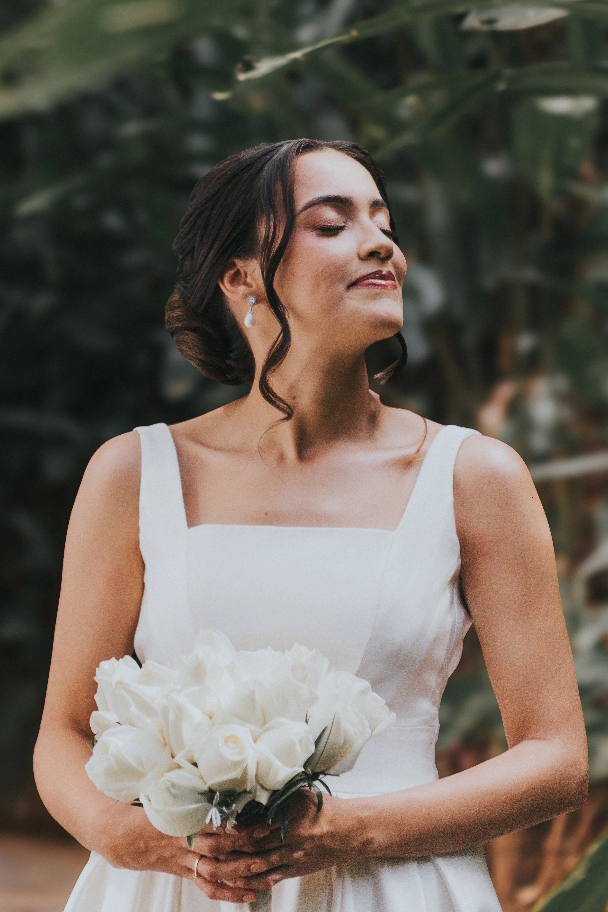casamento-belo-horizonte-retrato-noiva-01.jpg  Retrato de noiva de olhos fechados, com coque baixo e brincos de pérola, cercada pelo verde, casamento em Belo Horizonte