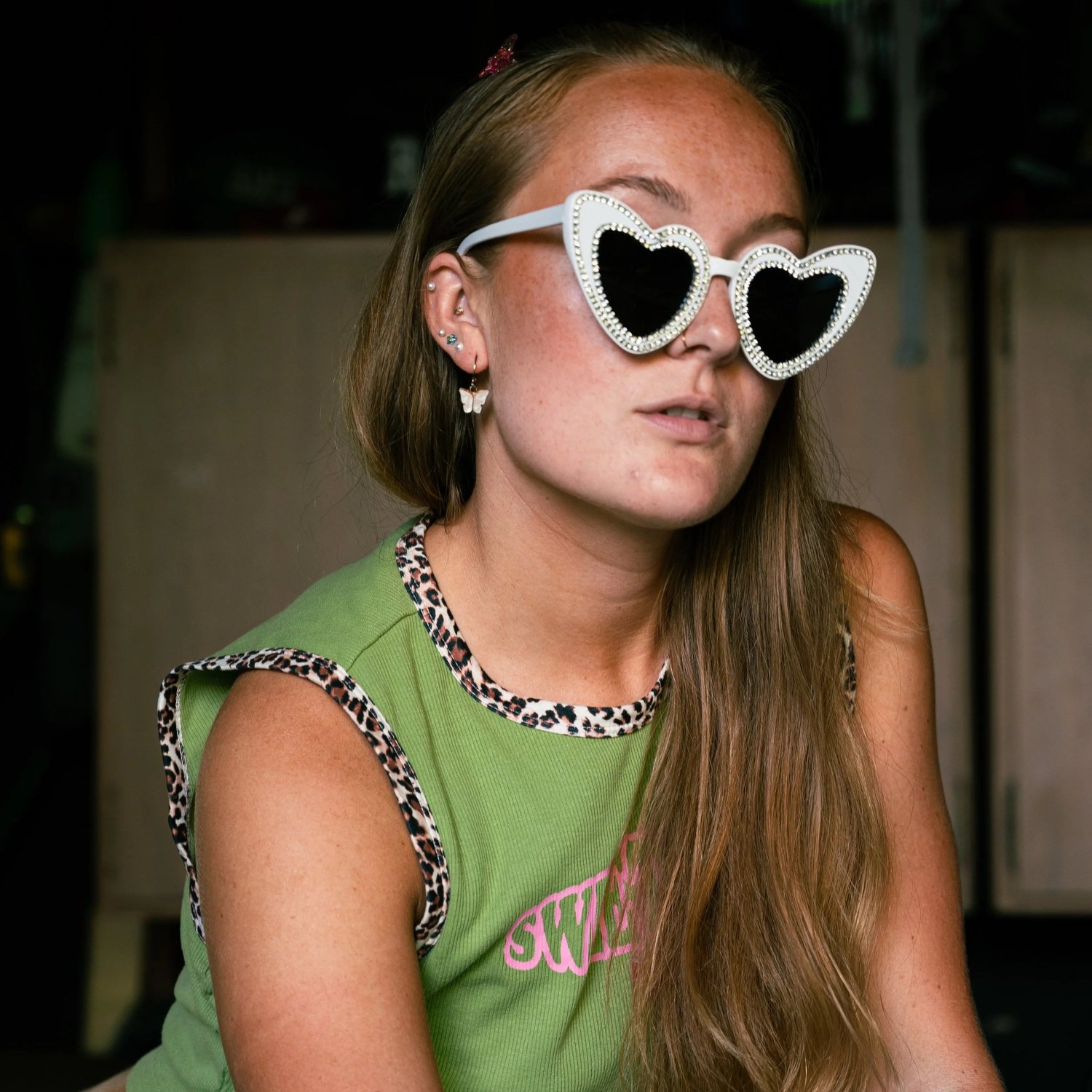 Editorial portrait of a woman in rhinestone heart-shaped sunglasses and layered earrings