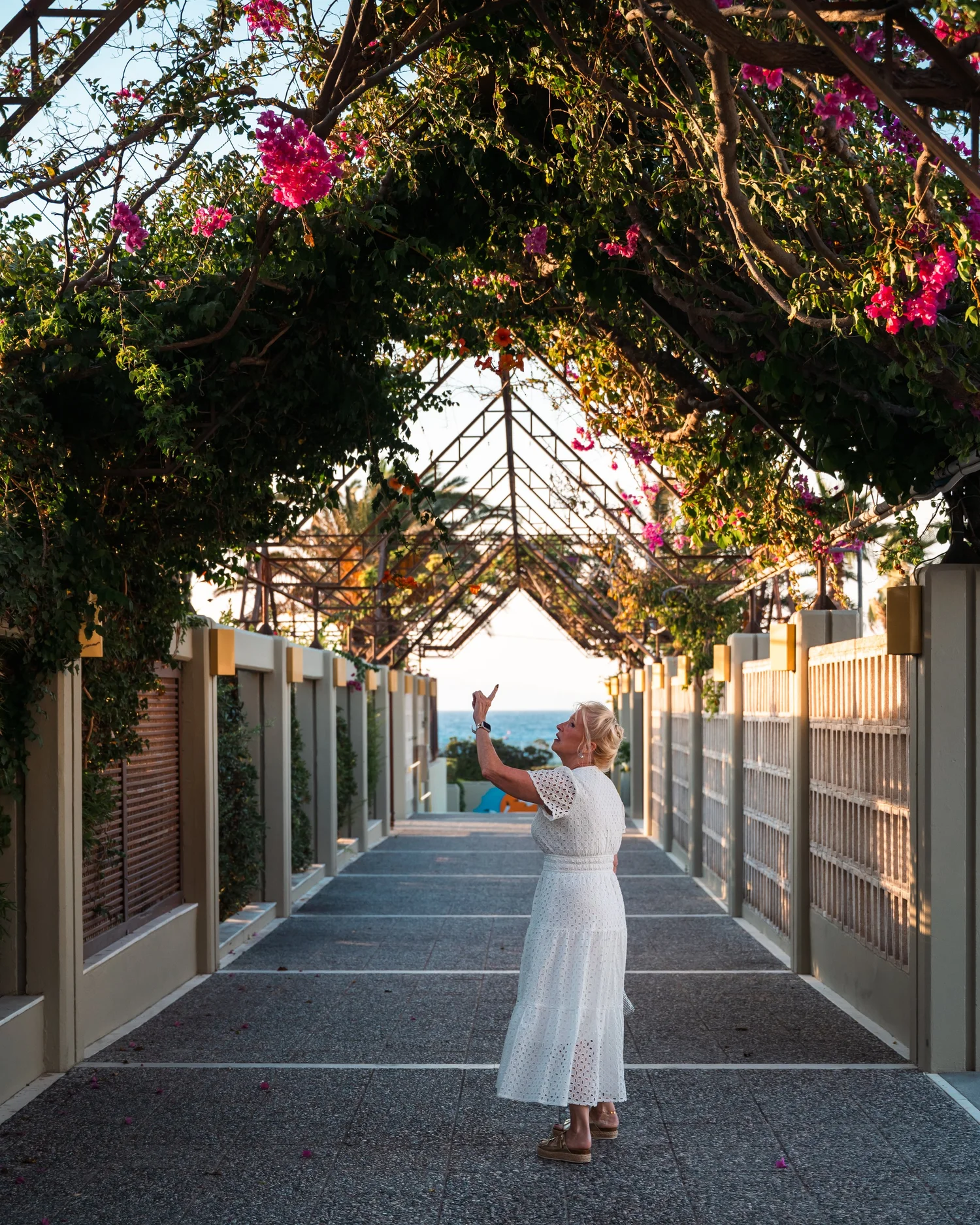 A woman in a white dress beneath an archway of pink flowering vines
