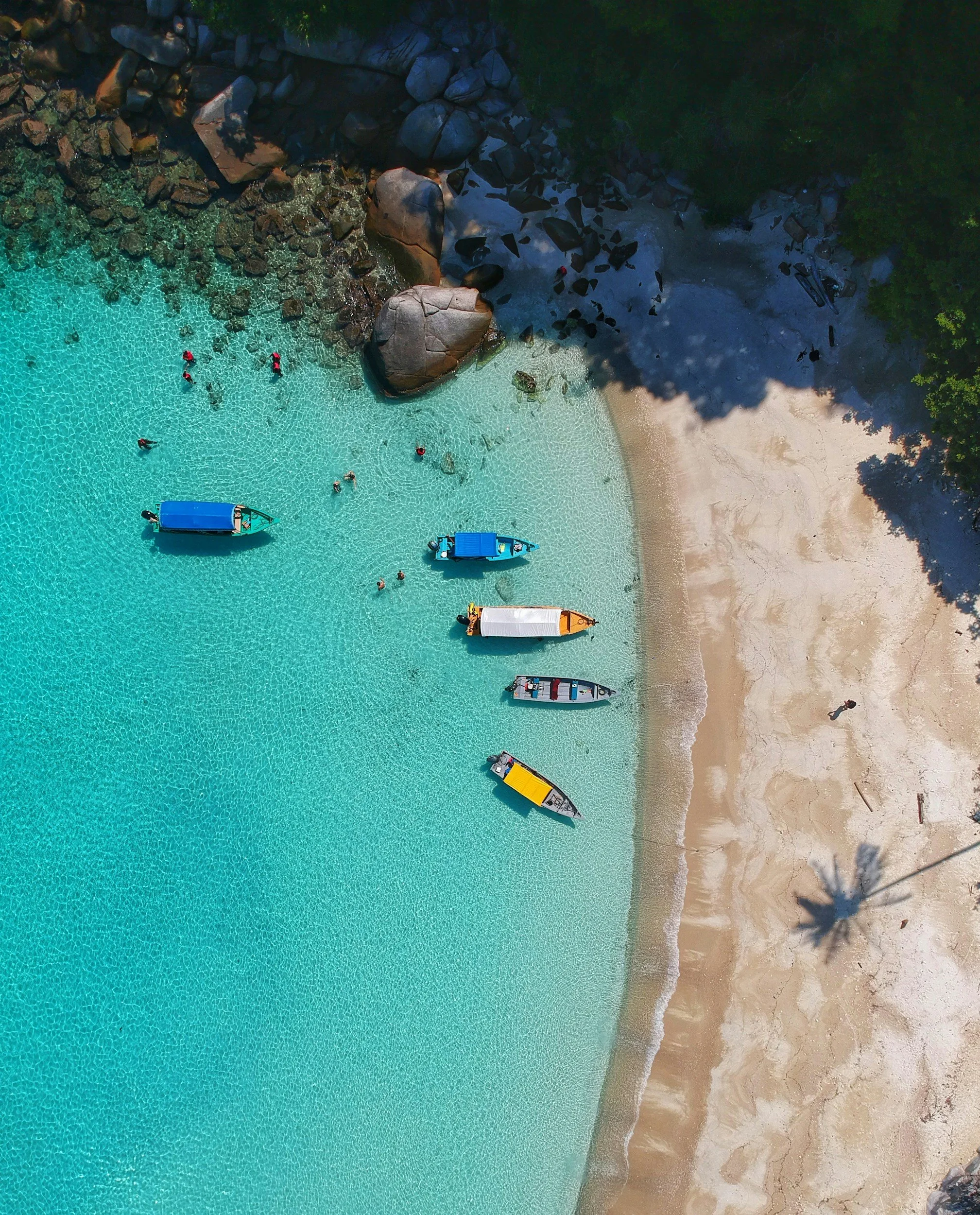 Aerial view of a beach with turquoise water, sandy shore, boats, and people swimming in the Dominican Republic, a location offering of the VWell Trip.