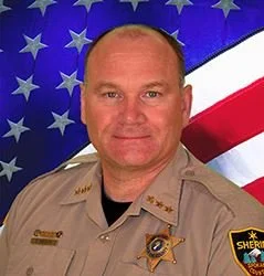 Portrait of a male sheriff's deputy in uniform in front of an American flag background.