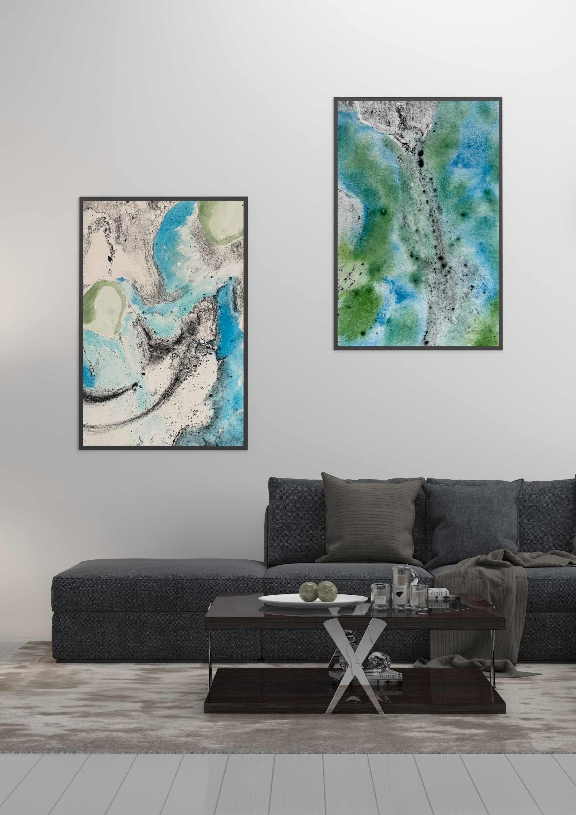 A modern living room with a dark gray sectional sofa, beige pillows, and a throw blanket. There are two abstract watercolor paintings with blue, green, and black on the wall. A dark wood coffee table with decorative objects and candles is in front of