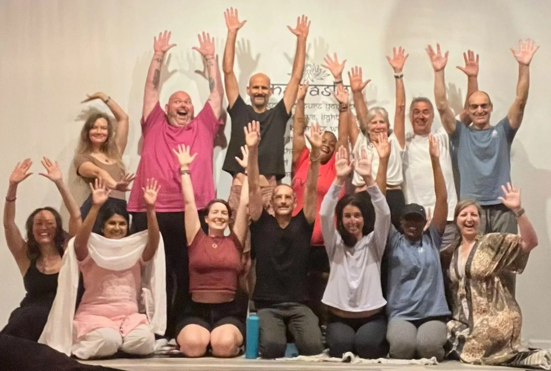 Group of people smiling, sitting and standing with hands raised in a room, possibly at a workshop or gathering.