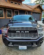 Black RAM pickup truck parked in front of a house with trees in the background.