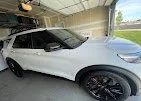 White SUV parked under a bridge with a grassy area and trees in the background.