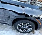 Close-up of the front corner of a black SUV, showing the tire, wheel, and part of the front bumper covered in snow.
