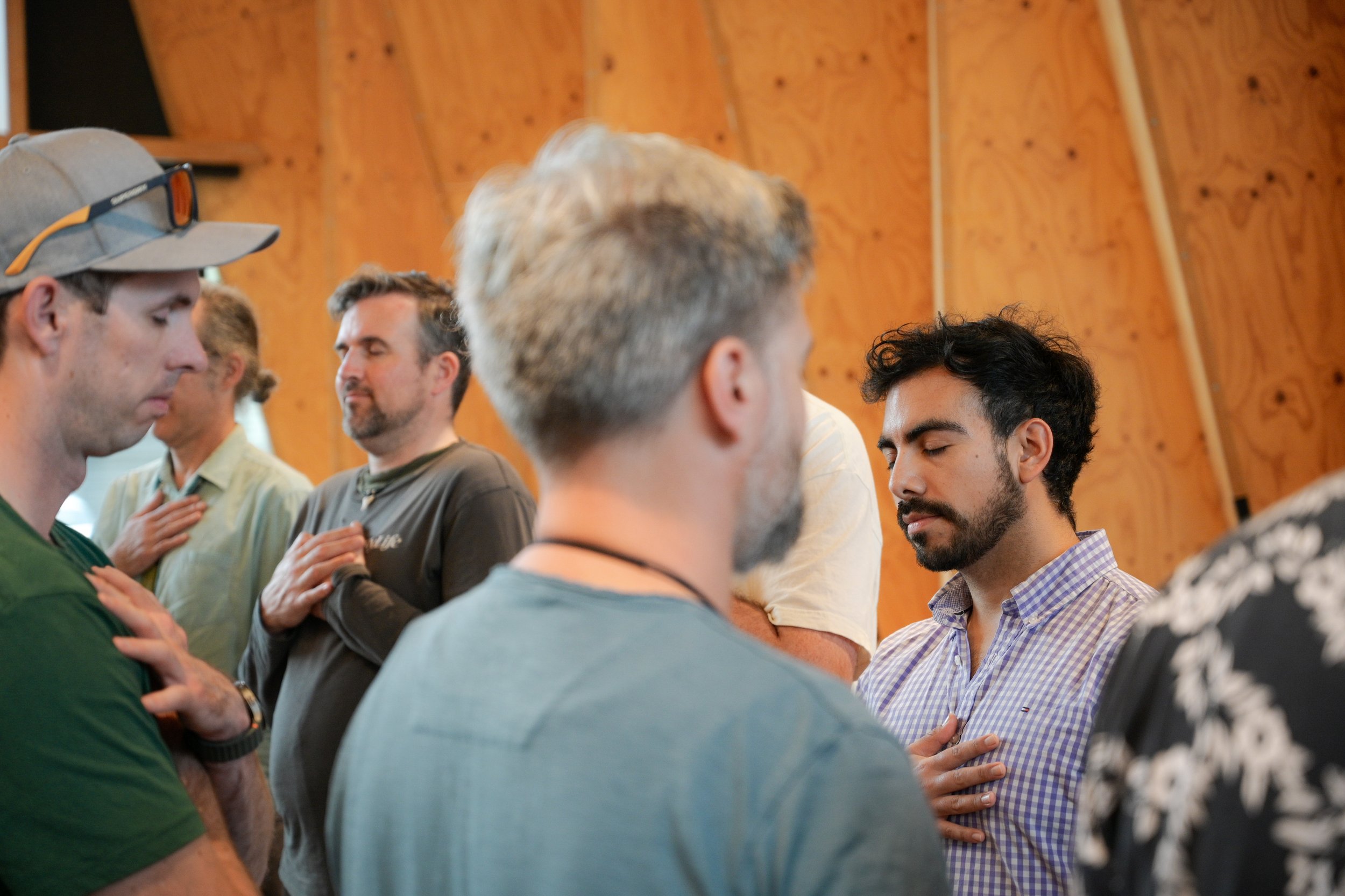 A group of people standing with their hands over their hearts, participating in a gentle moment of silent connection, in a room with wooden walls.