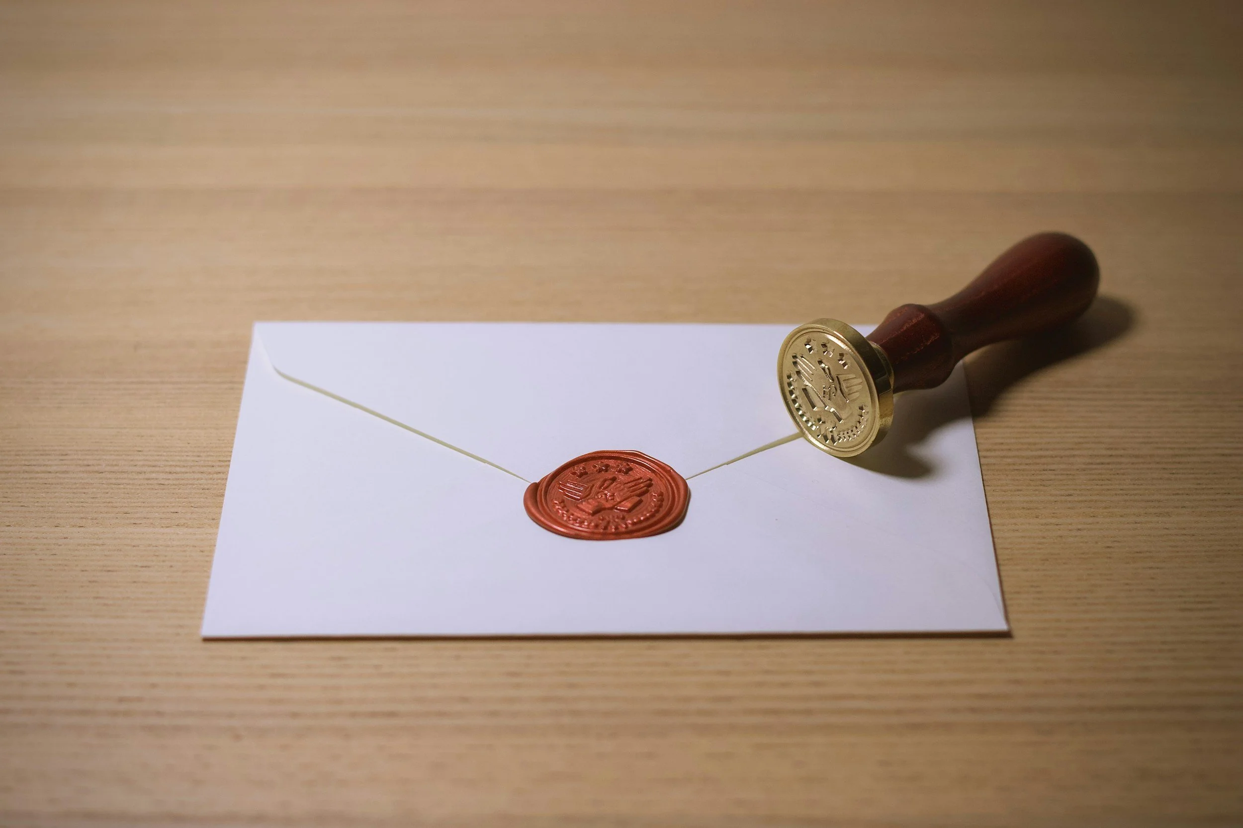 An envelope with a red wax seal and a stamp, placed on a wooden surface.