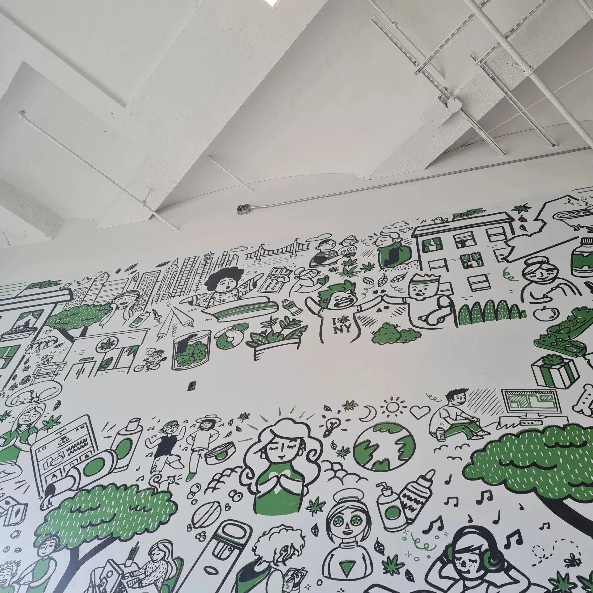 Colorful mural on a white wall depicting people, cityscape, nature, and marijuana-related imagery in a cartoon style with green, black, and white colors.
