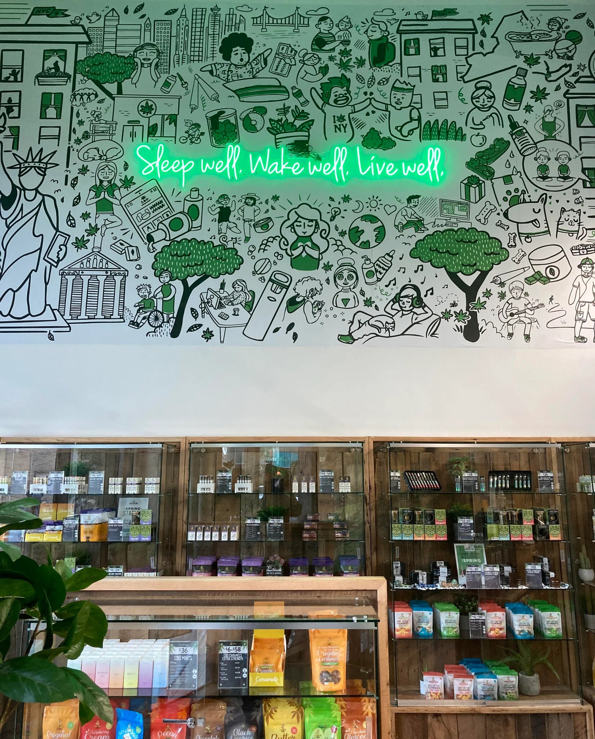 Colorful illustrated mural with green neon sign reading "Sleep well. Wake well. Live well," featuring various people engaging in activities such as exercising, working, relaxing, and socializing, with urban and nature elements.