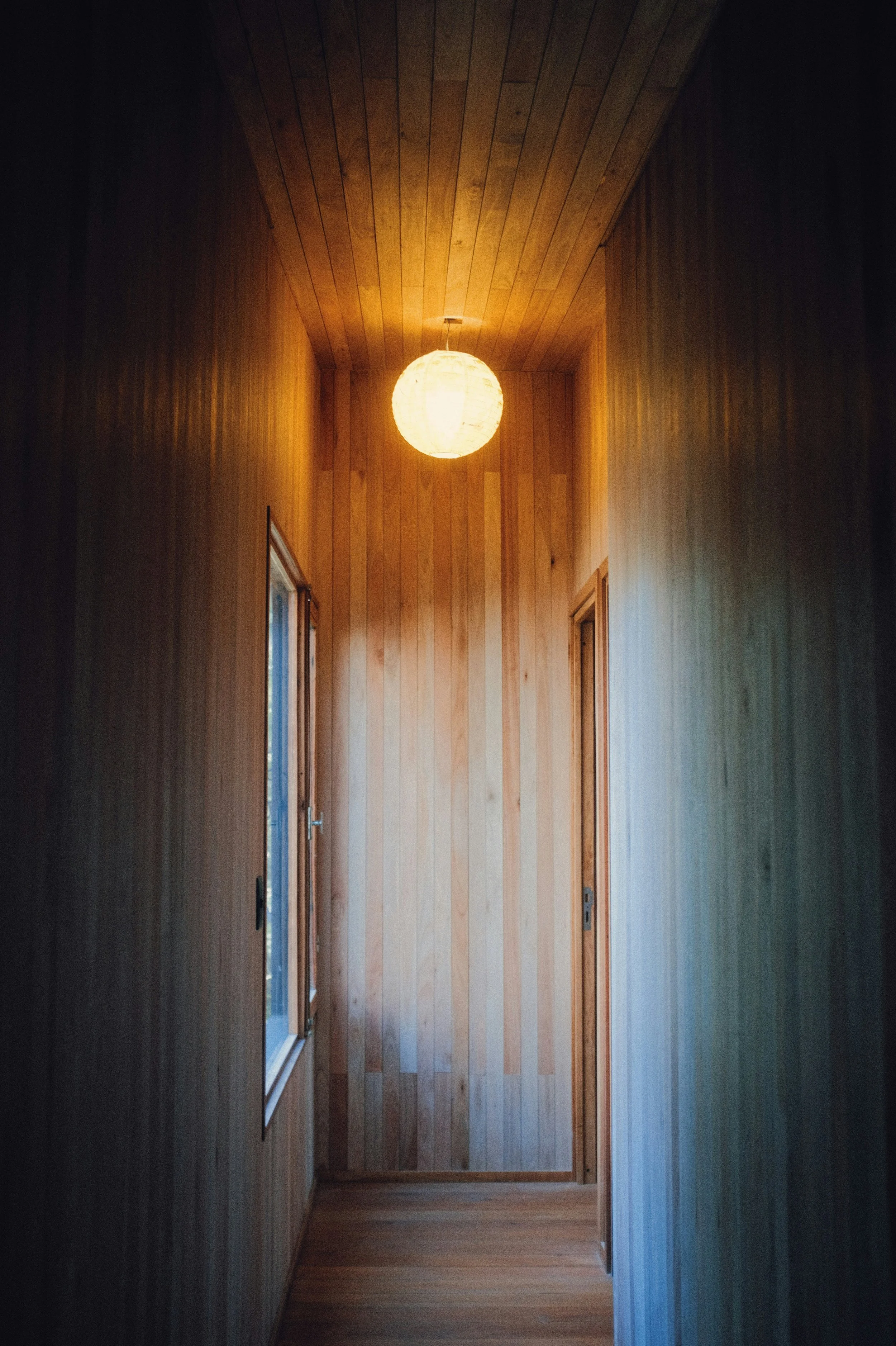 Wood-paneled hallway with a round paper lantern ceiling light and small windows on the left side