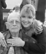 A young woman and an elderly woman smiling and sitting close together.
