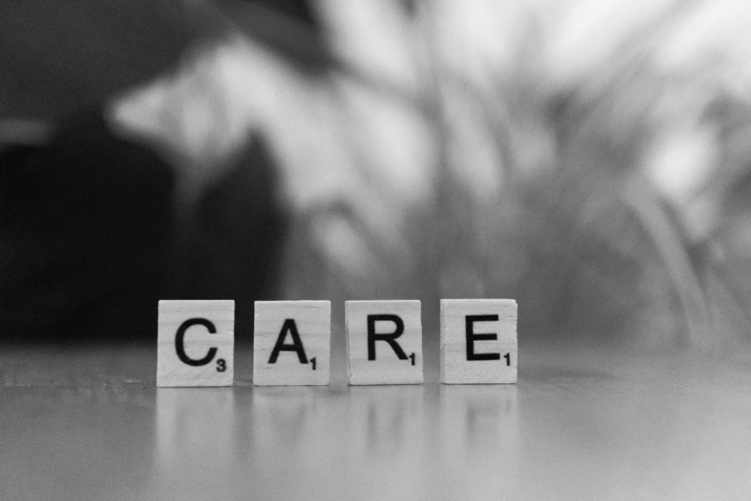 Scrabble tiles spelling the word 'CARE' in black letters on wooden blocks on a flat surface, with a blurred background.