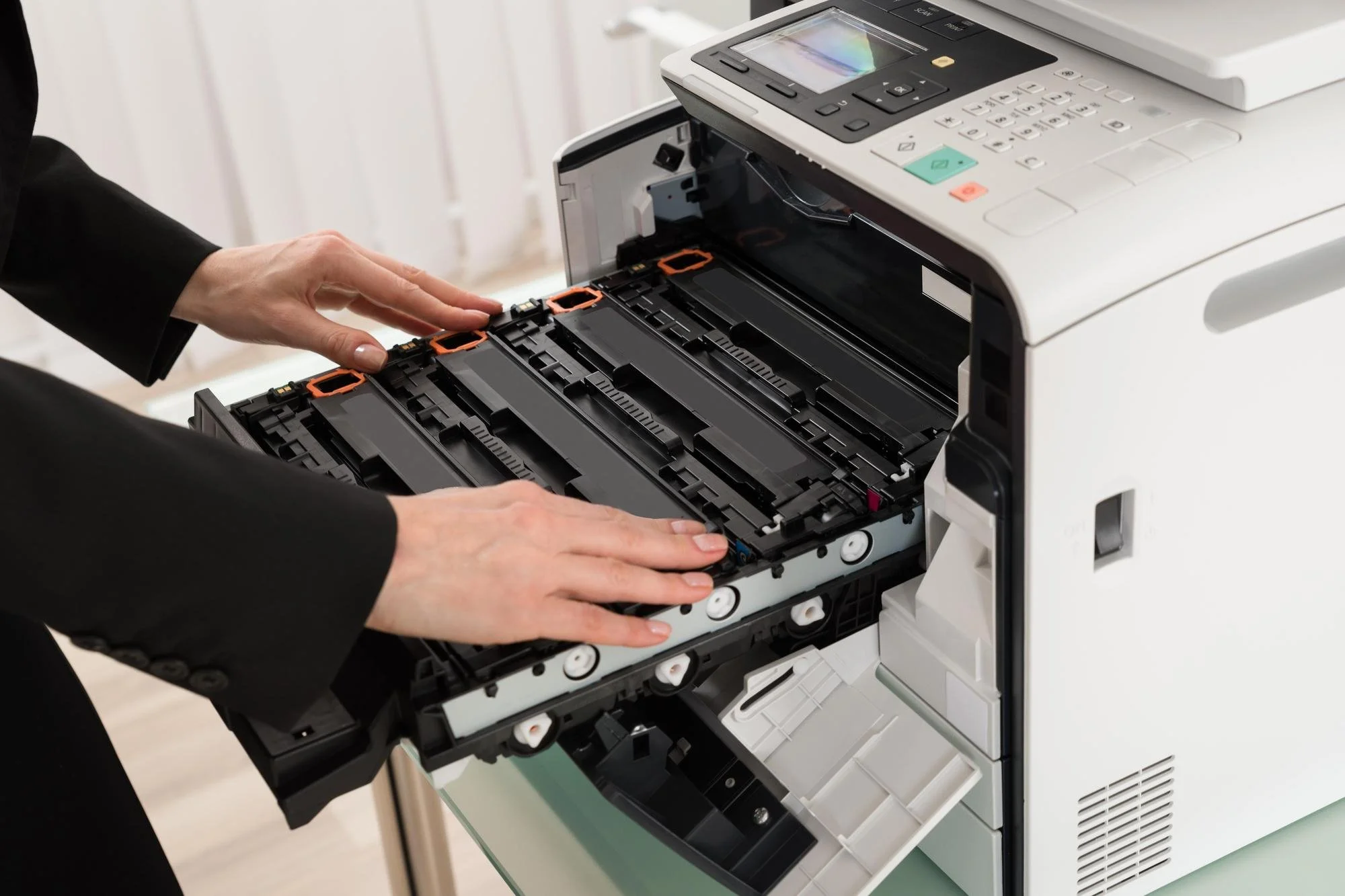 Person in black suit opening the internal components of a multifunction printer or copier, revealing the toner cartridges and internal mechanisms.