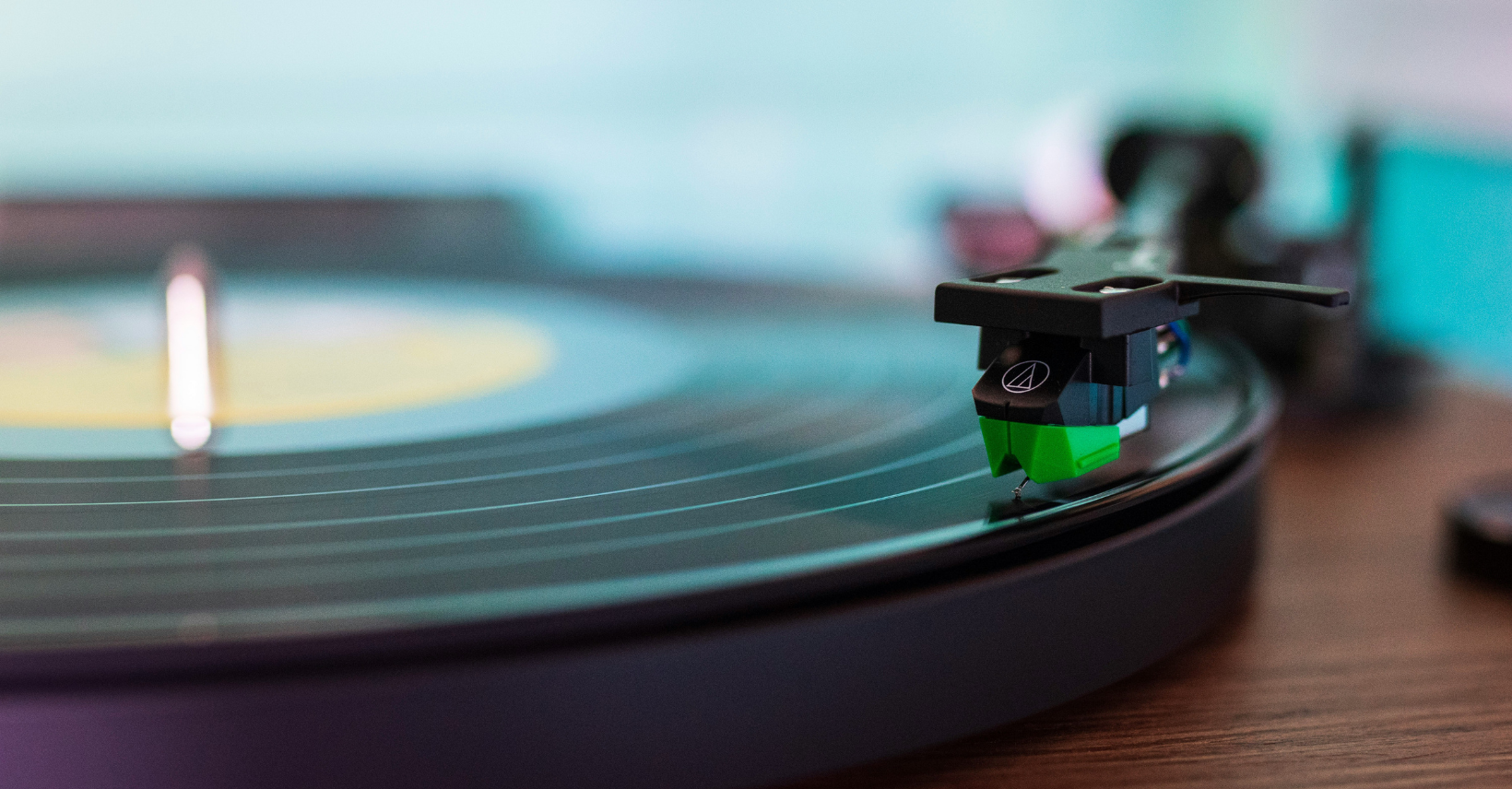 close-up photograph of a black vinyl record and a black and green stylus on a turntable