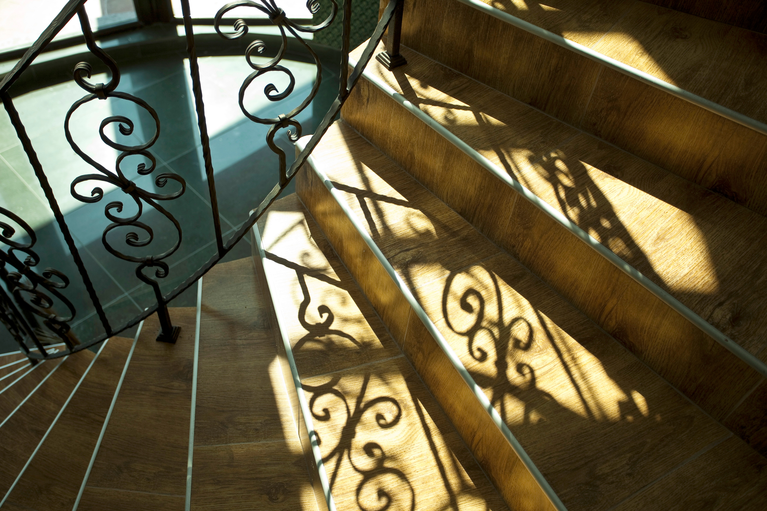 streams of sunlight and shadow on a spiral staircase with a decorative wrought iron railing