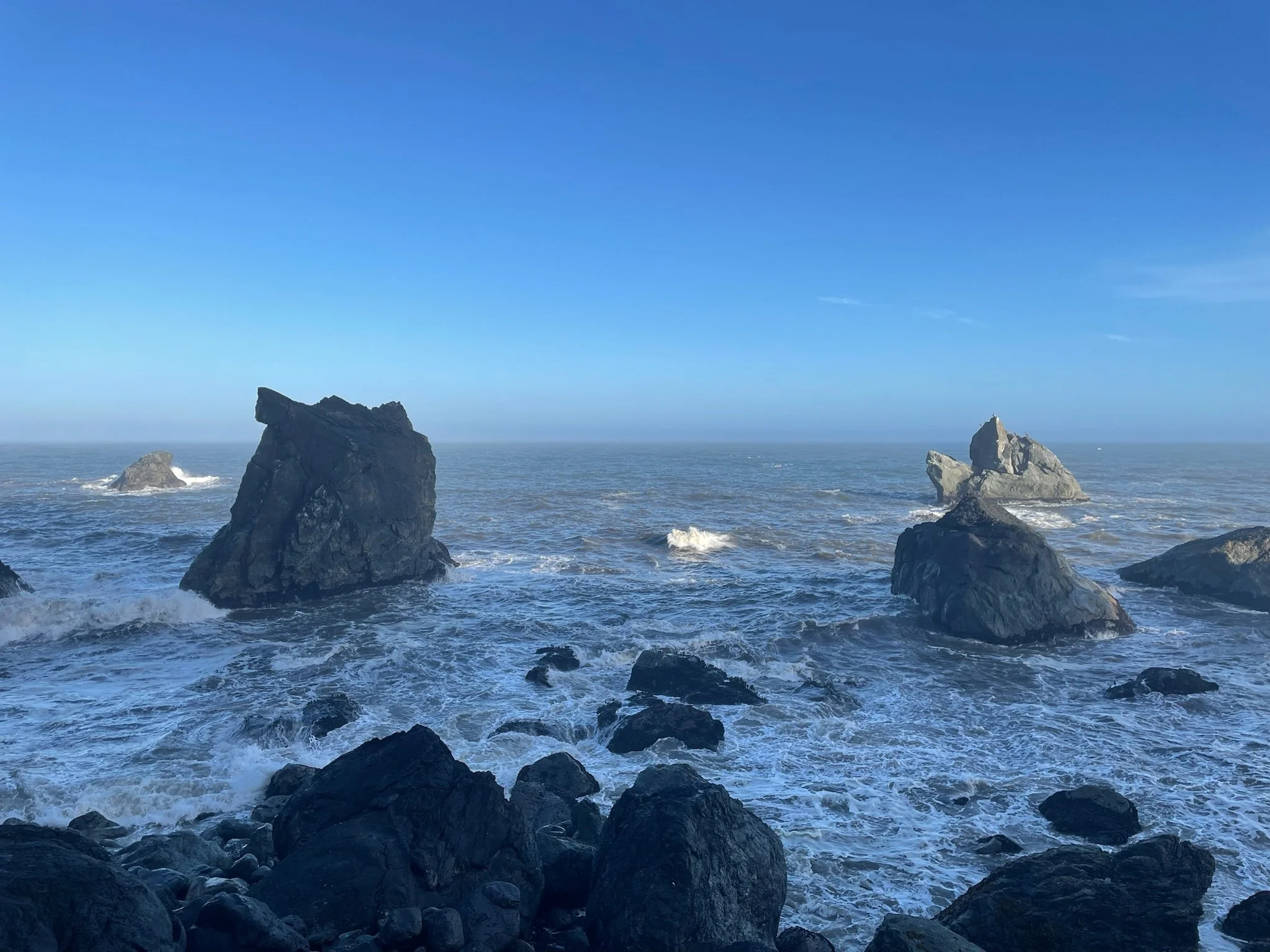 Rocky shoreline with large rocks in the ocean and a clear blue sky