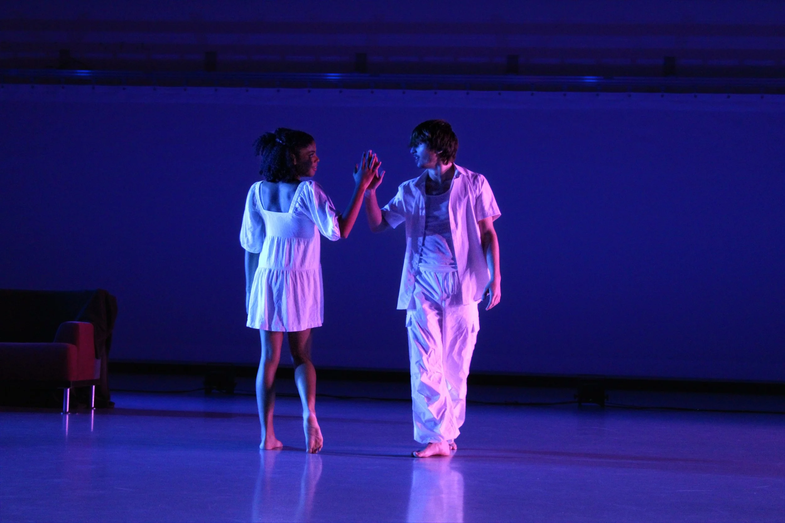 Two people, a woman and a man, dancing on a stage with purple and blue lighting. They are giving each other a high five.