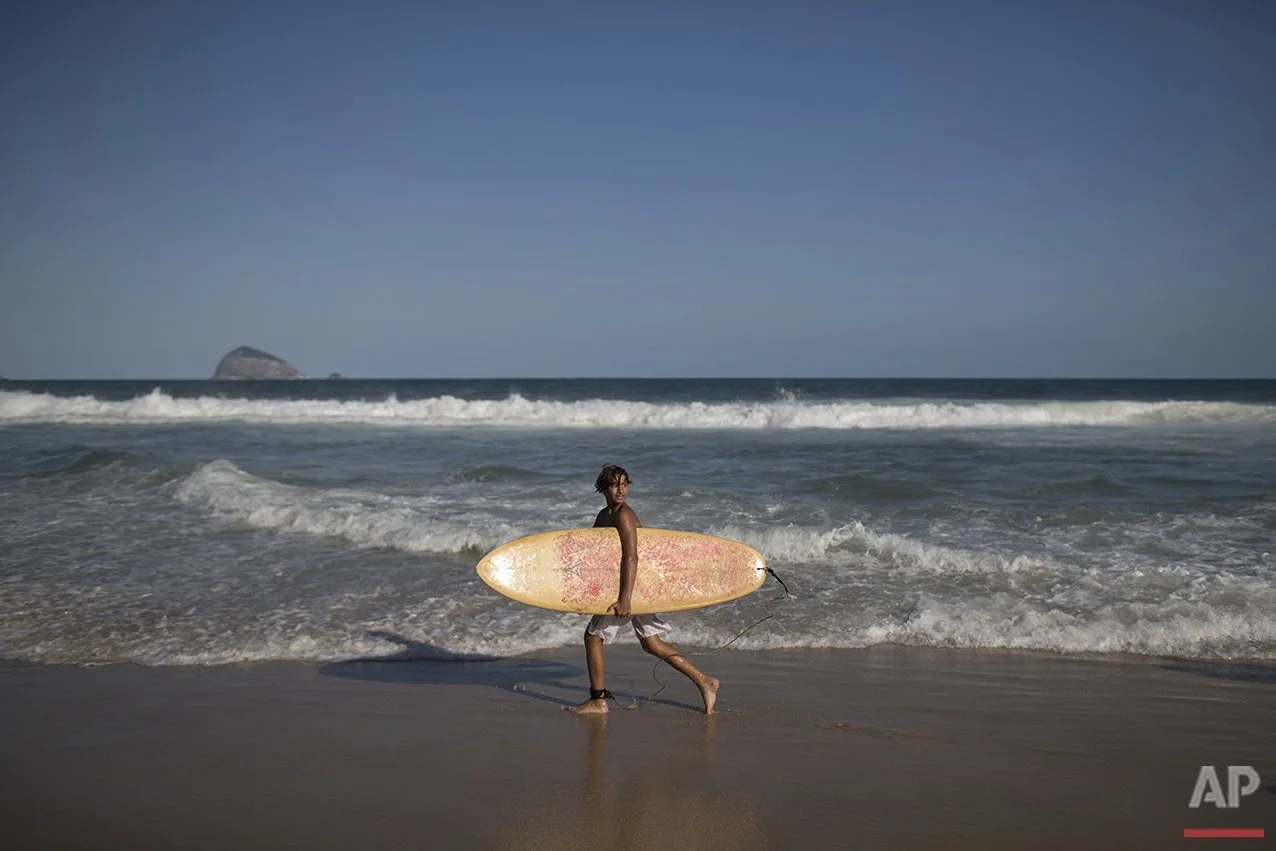 A young person walking along the beach at sunset, holding a surfboard.