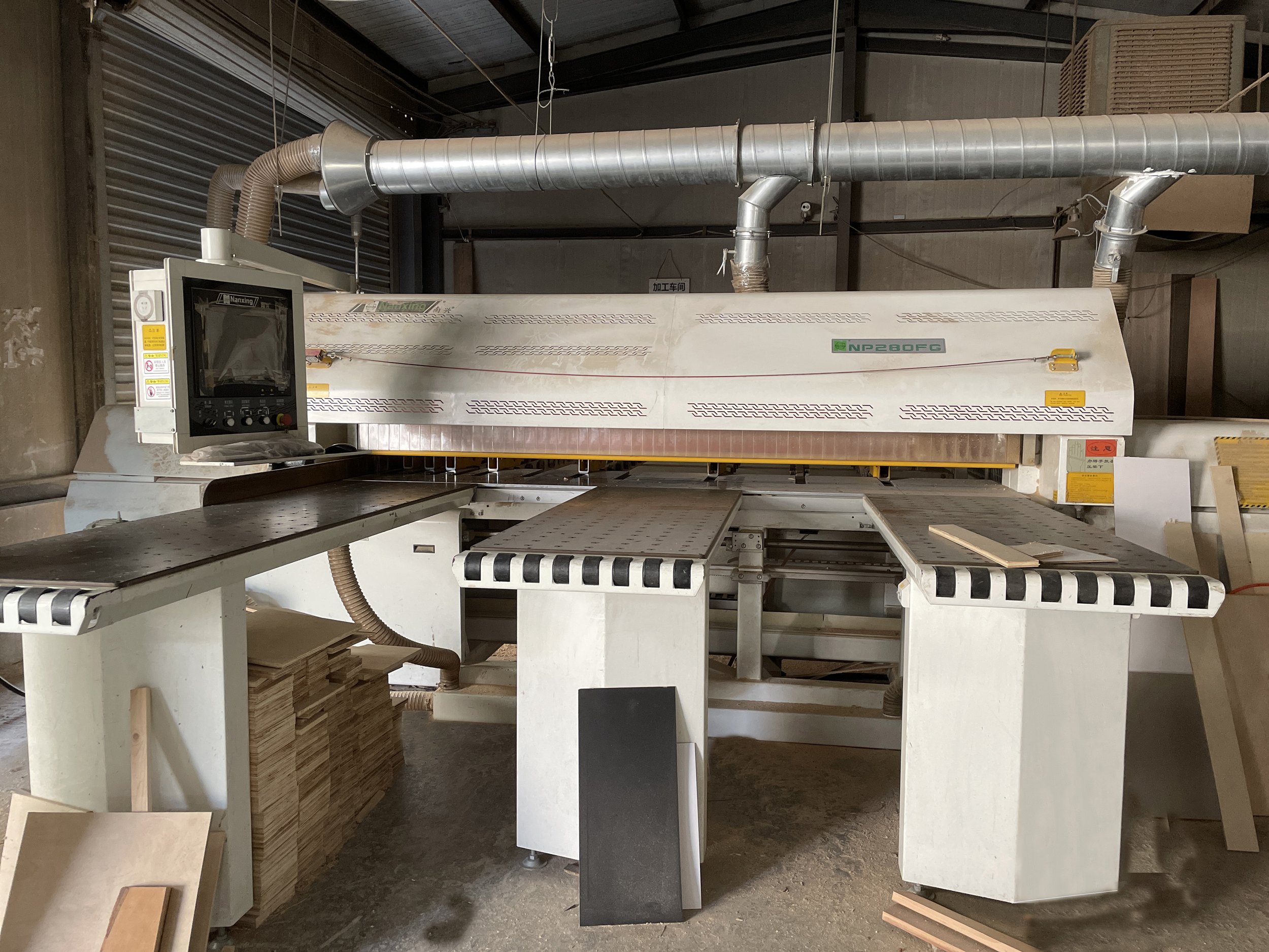 Large industrial woodworking machine in a workshop, with conveyor table and dust extraction hoses surrounding it.