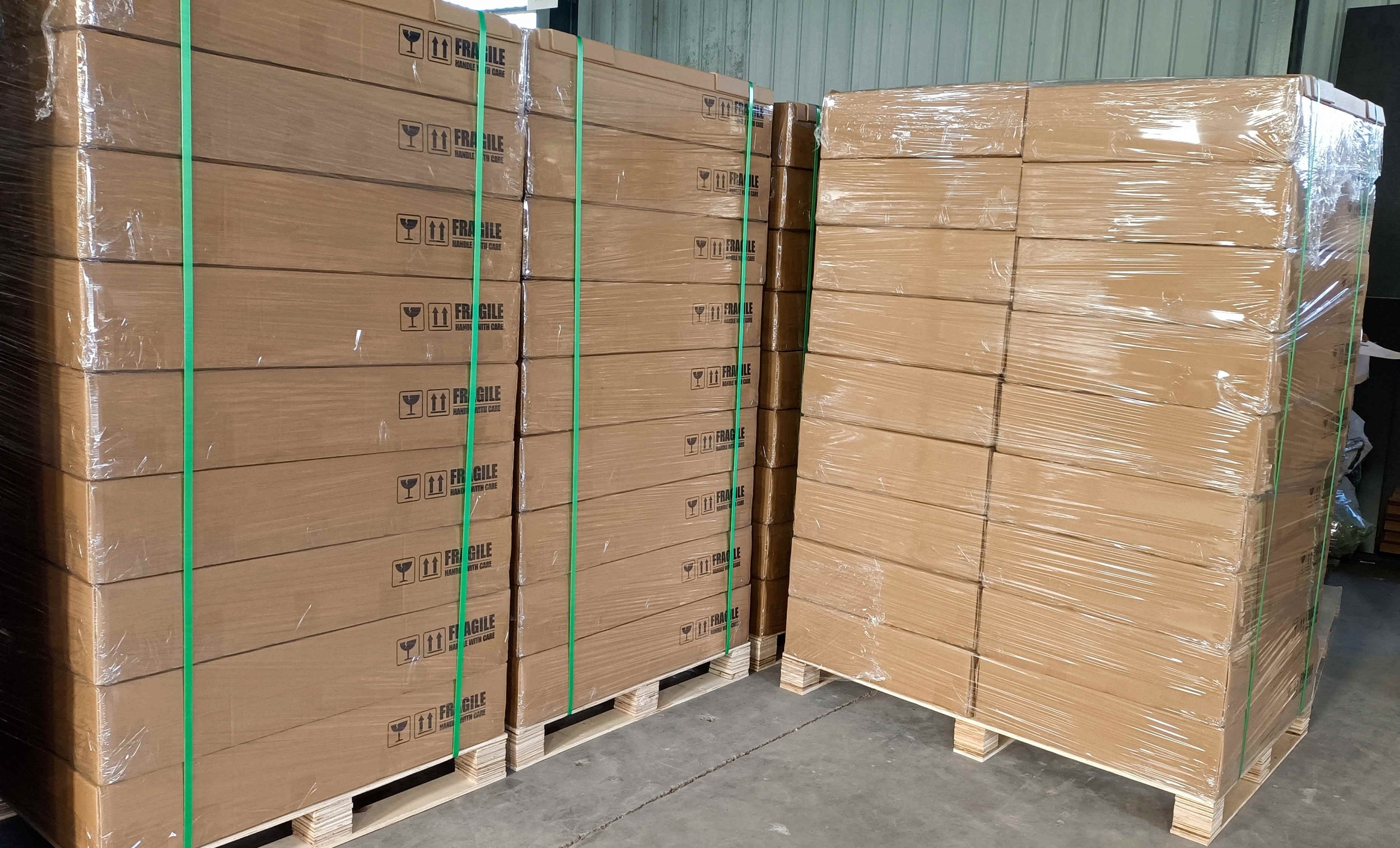 Stacks of large cardboard boxes wrapped in plastic on wooden pallets in a warehouse.