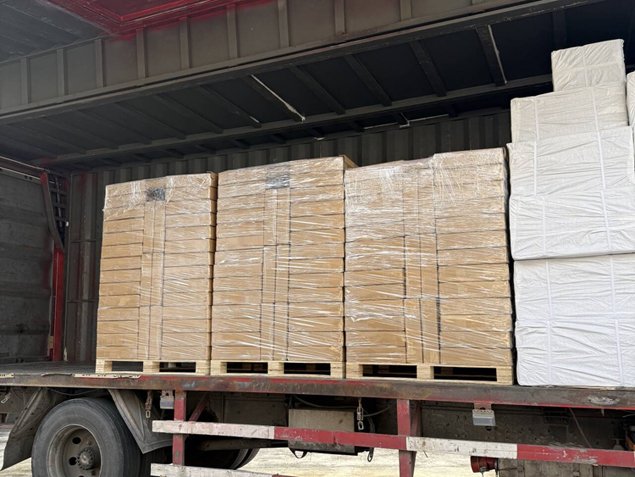 Large pallets of packaged wooden boards and white wrapped materials loaded on a flatbed truck in a warehouse.