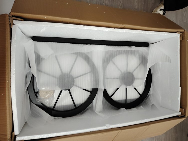 Two black fans with protective grills, packed in white foam and tissue paper inside a cardboard box for shipping.