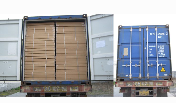 Open shipping container filled with stacked cardboard boxes, parked next to a closed blue shipping container.