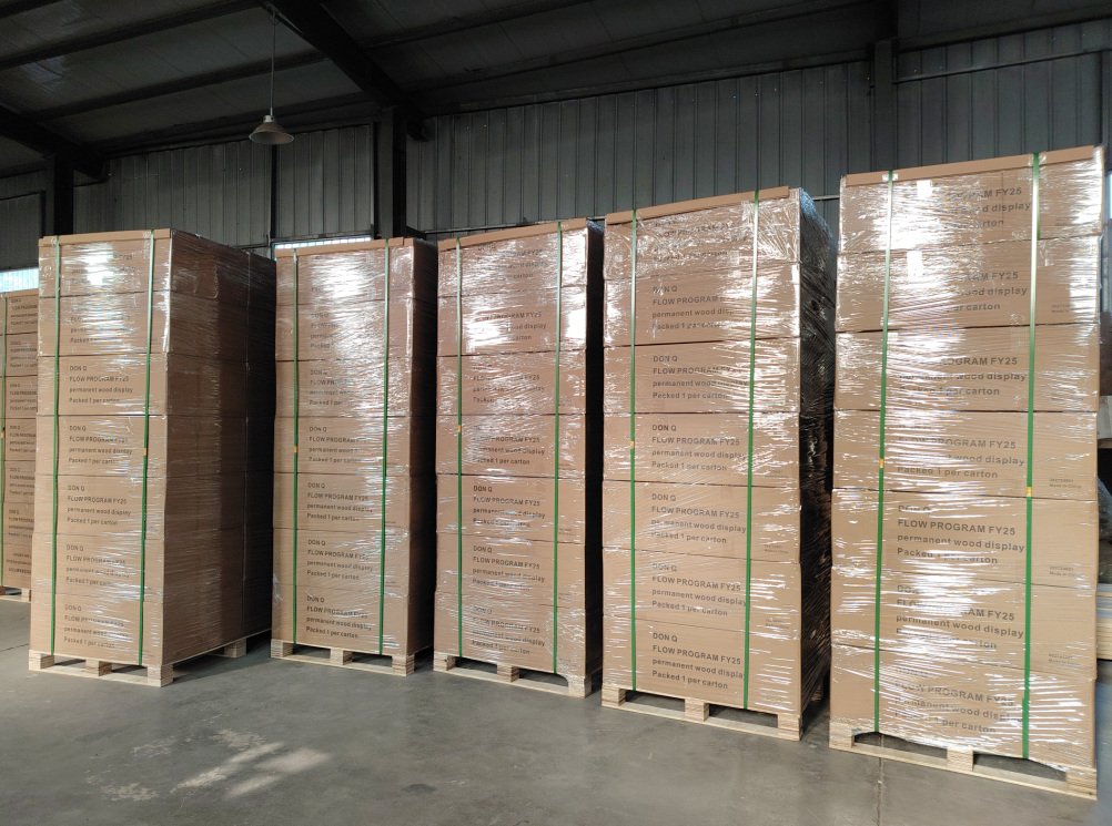 Five large pallets of packaged wood display boards wrapped in plastic, stored inside a warehouse.