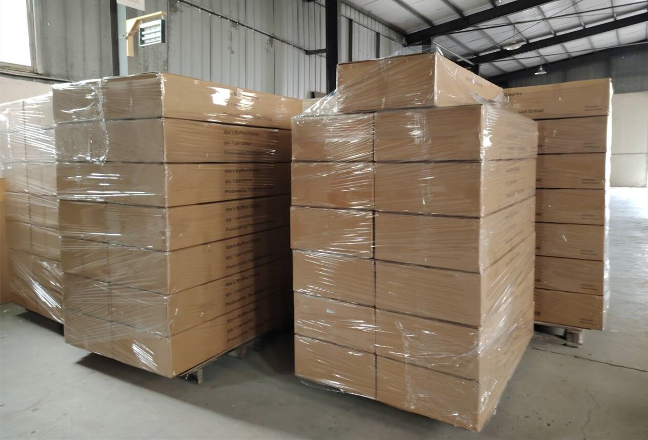 Stacks of cardboard boxes wrapped in plastic on pallets inside a warehouse.