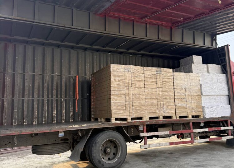 Flatbed truck with stacks of cardboard and white packaging materials loaded inside a metal shipping container