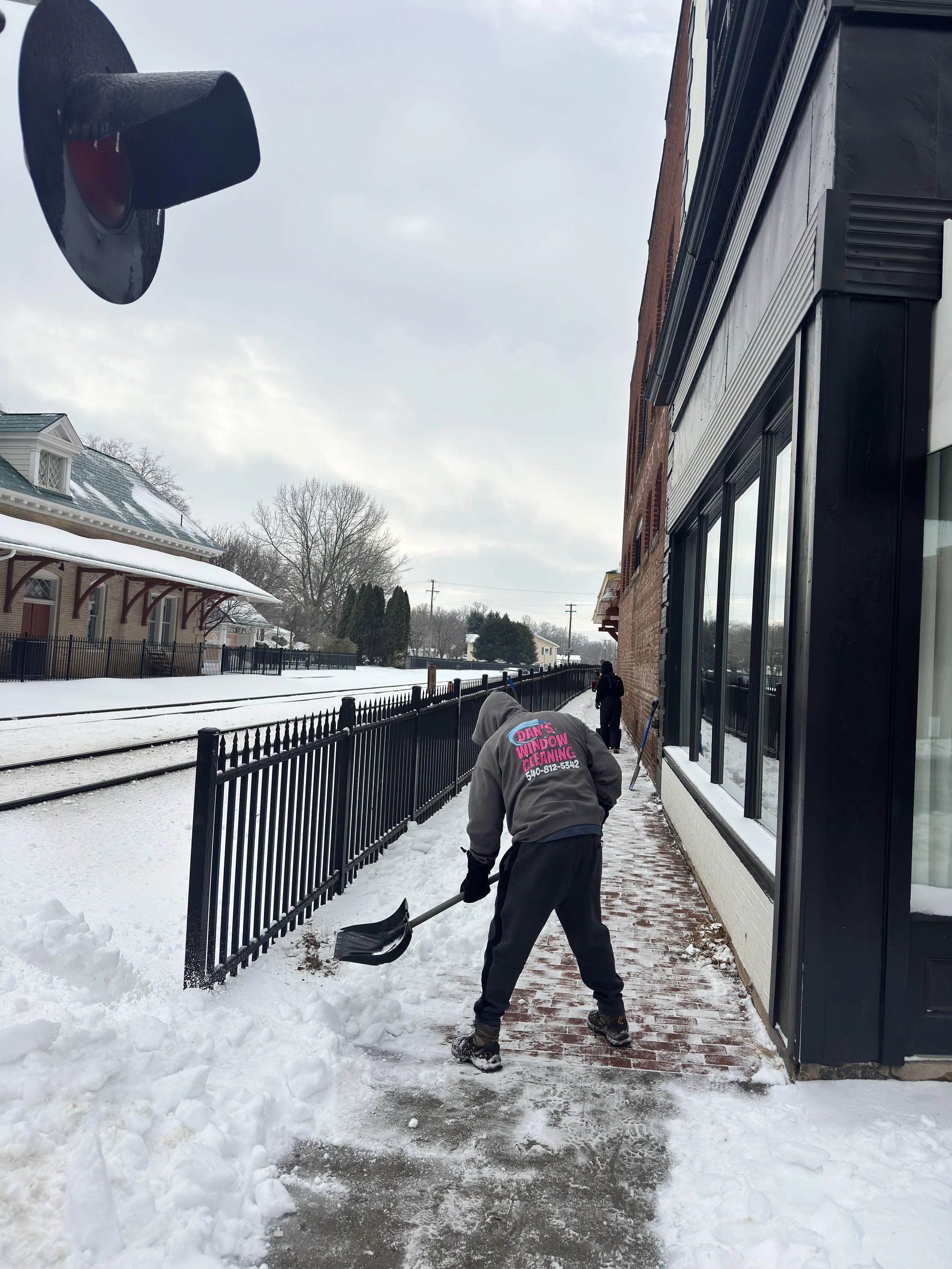A man using a shovel to remove snow off a sidewalk.
