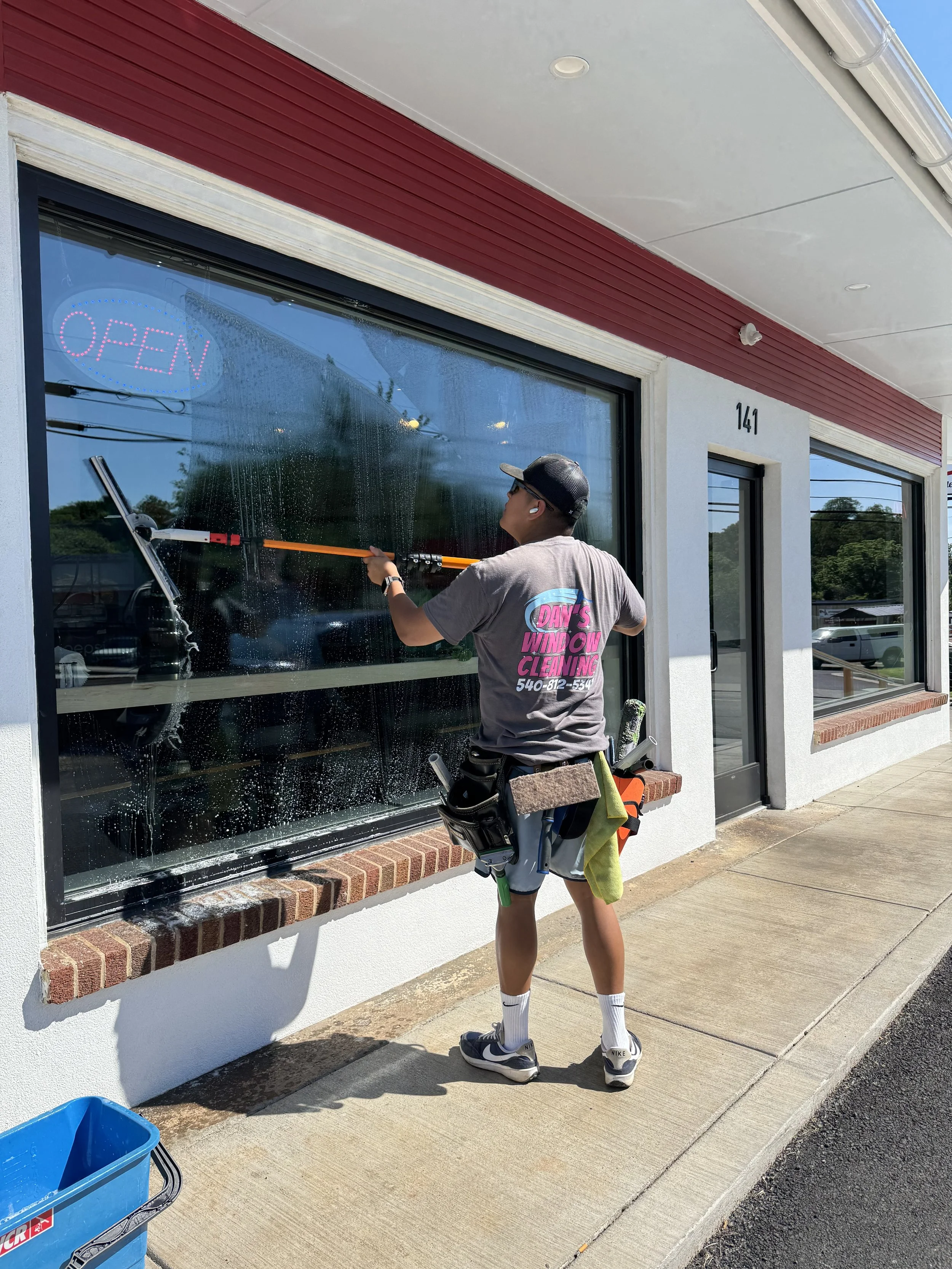 A young man using a pole and squeegee to clean a large window on a commercial building's exterior.