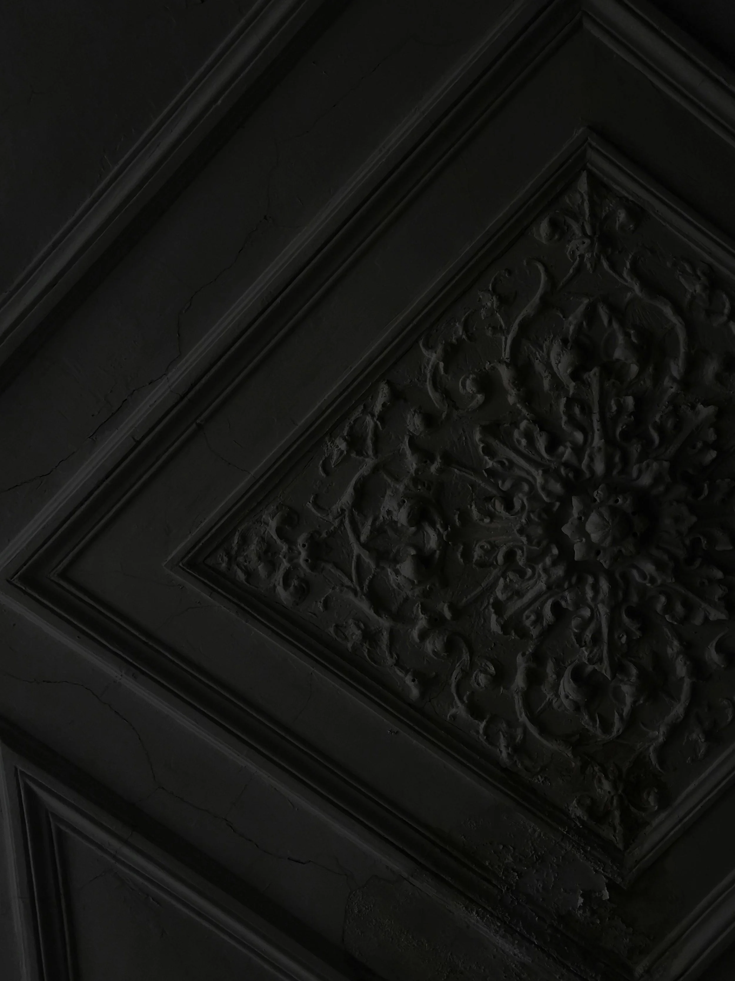 Dark, ornate ceiling with decorative molding and intricate detailing, showing signs of age with some cracks.