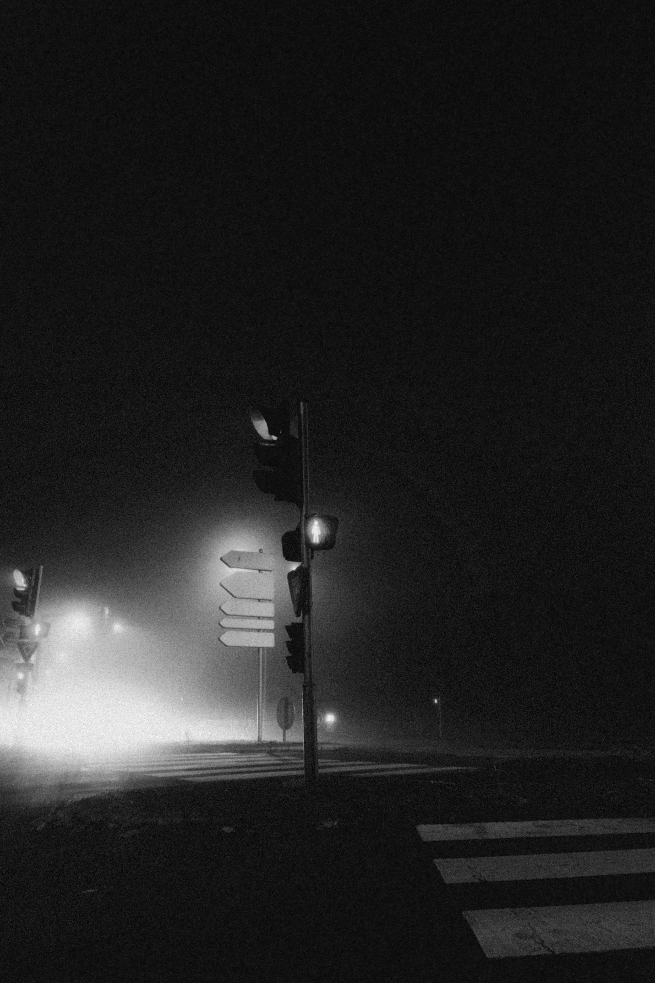 Night scene at a foggy intersection with traffic lights, street signs, and a pedestrian crosswalk.