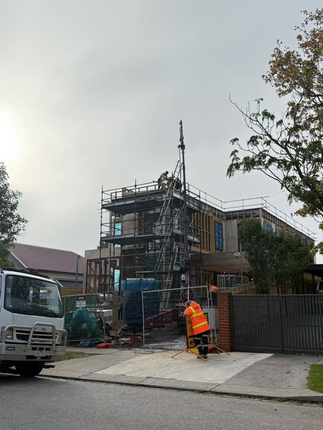 Construction workers in high-visibility clothing working on a multi-story building under construction, with scaffolding and construction equipment around.