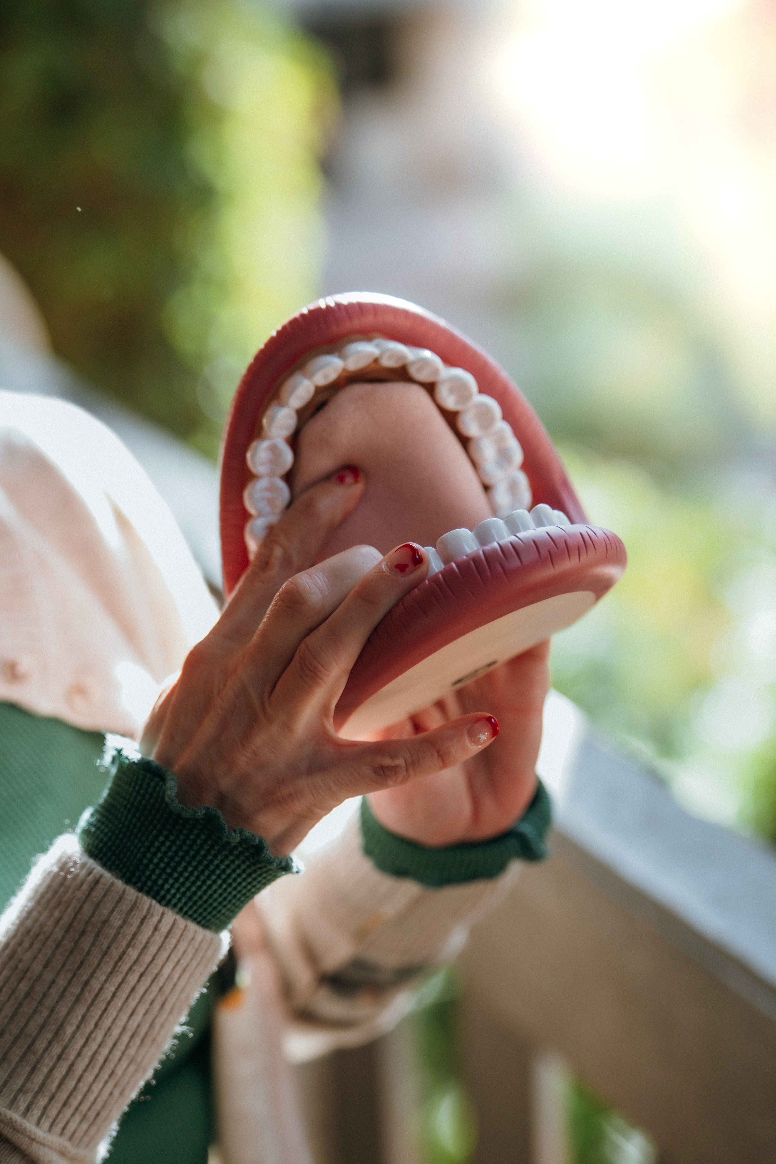 Person holding a large plastic model of a human mouth with teeth, abstract background.