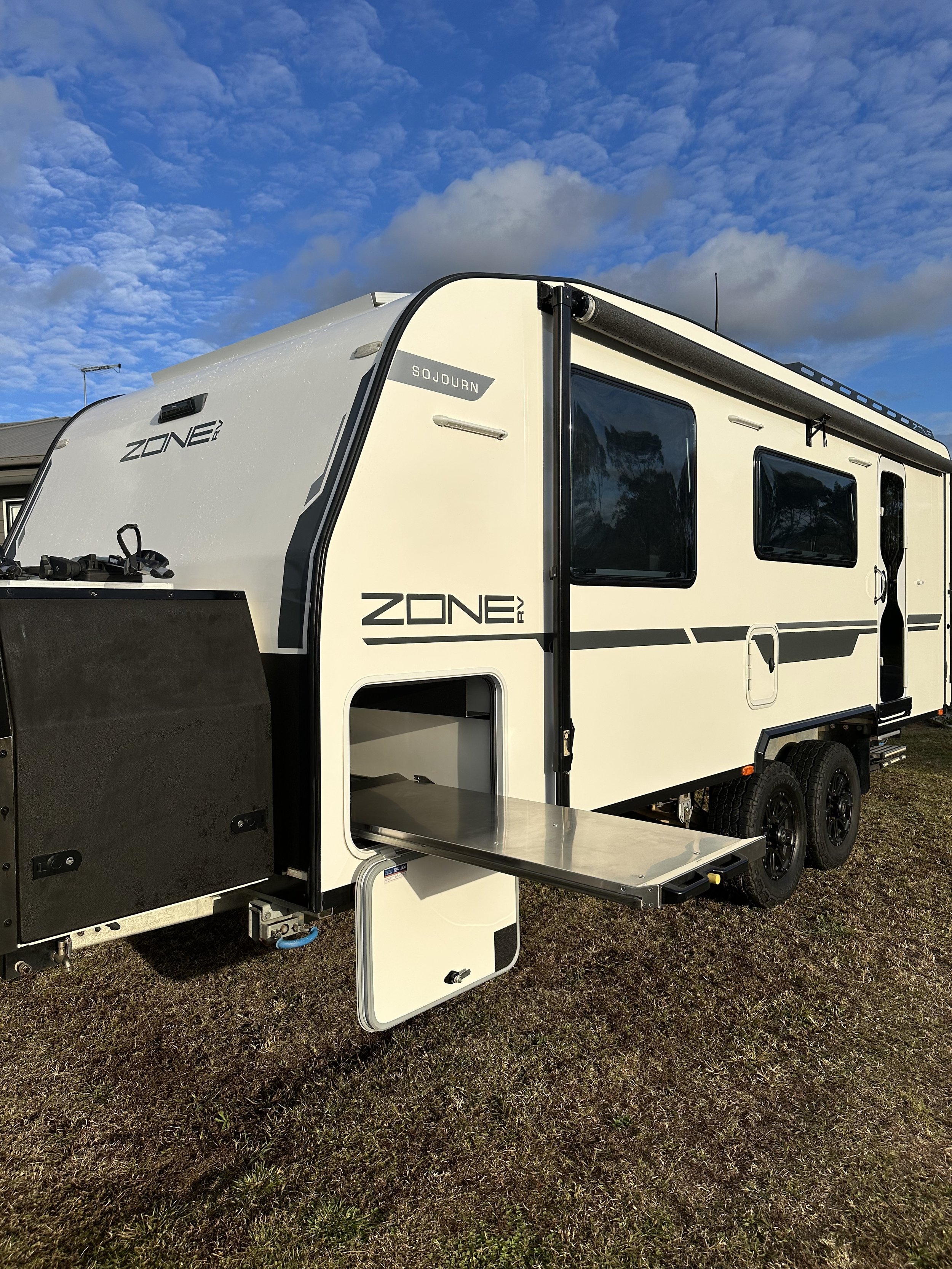 A white caravan with black accents parked on grass under a partly cloudy sky.